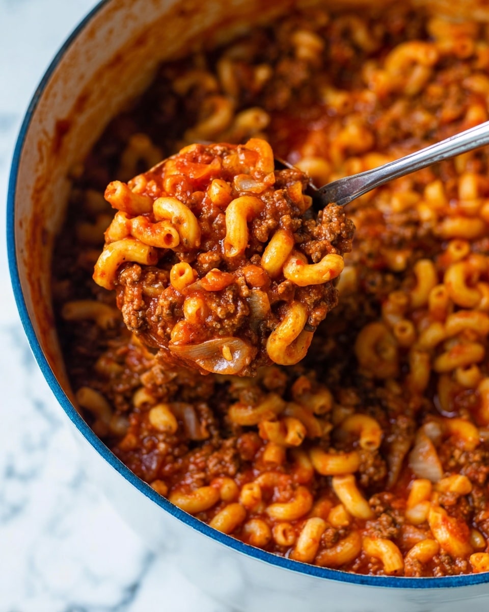 A close-up of a large white pot filled with a thick, hearty mixture of elbow macaroni pasta and ground meat in a rich, red tomato sauce. The pasta is soft and coated well with the sauce, along with small pieces of onions visible throughout. A large silver ladle is scooping up a serving from the pot, showing a dense cluster of the pasta and meat sauce, highlighting the texture and color contrast between the red sauce, brown meat, and pale pasta. The pot sits on a surface with a white marbled texture, and the overall look is warm and comforting. Photo taken with an iphone --ar 4:5 --v 7