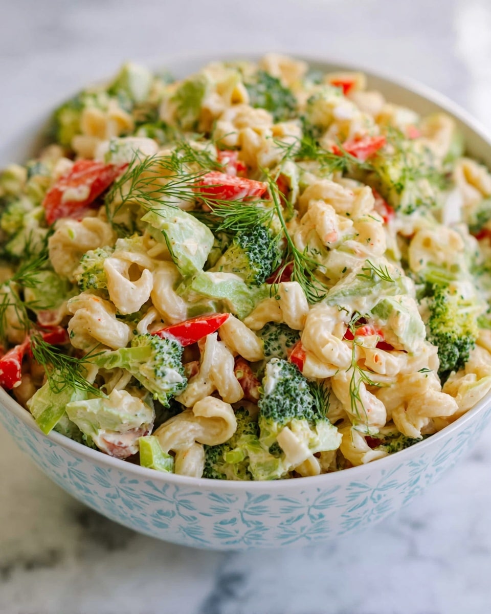 A bowl filled with a creamy pasta salad showing about three layers: the bottom layer is a mix of small curved pasta pieces in light beige, the middle layer has chopped green broccoli and light green lettuce mixed with thin white onion slices, and the top layer is scattered with bright red bell pepper chunks and green dill sprigs. The bowl is white with soft blue patterns, sitting on a white marbled surface. The salad looks fresh and colorful with a mix of smooth and crunchy textures. photo taken with an iphone --ar 4:5 --v 7
