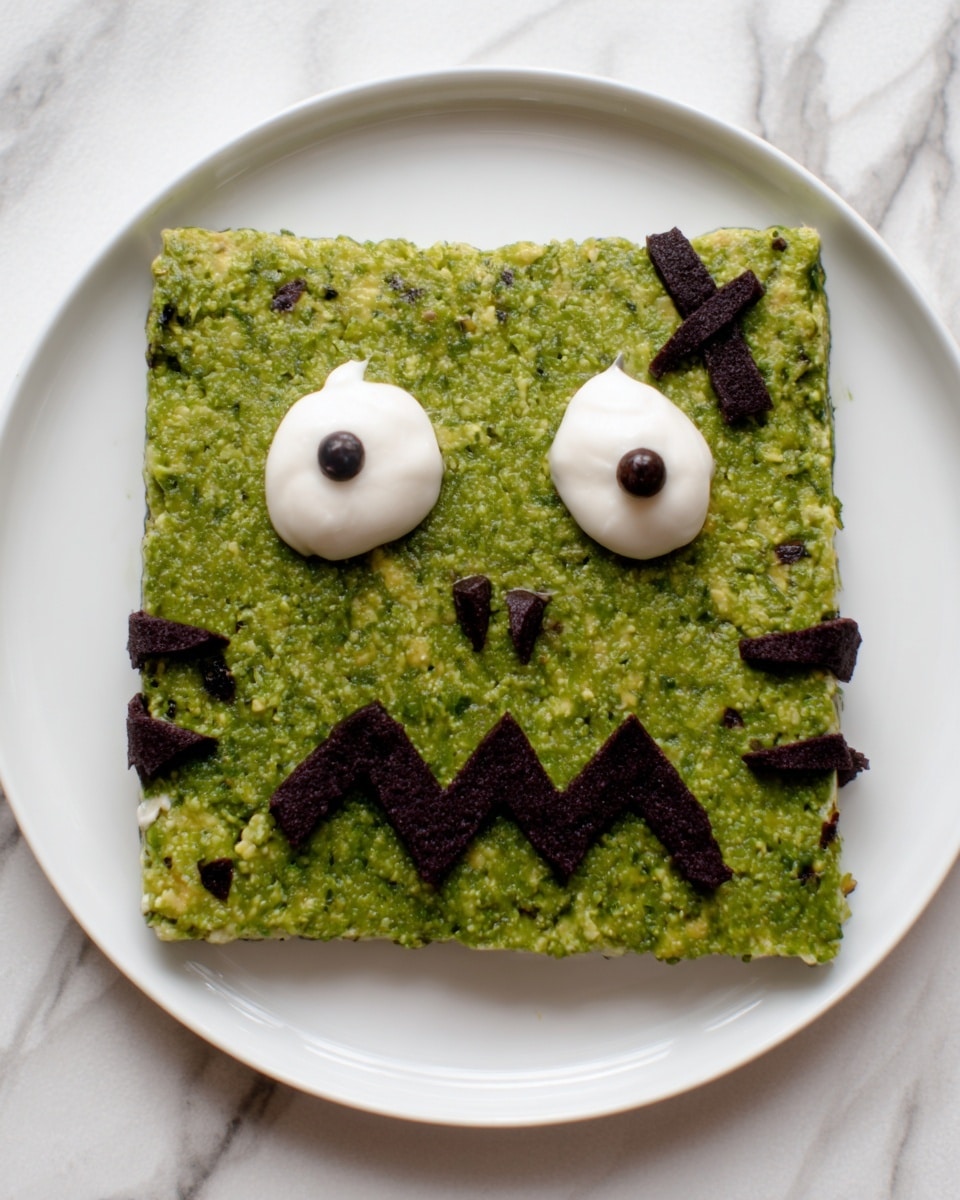 A square green spread made from a chunky mixture with small bits of darker colors is placed on a white plate. On top, two dollops of white cream with small dark spots and a larger dark spot between them form eyes and a nose. Below these, dark zigzag lines create a mouth, while more dark pieces are arranged on each side at the bottom and a set of short lines on the upper right create an appearance like stitches. The plate sits on a white marbled surface. Photo taken with an iphone --ar 4:5 --v 7