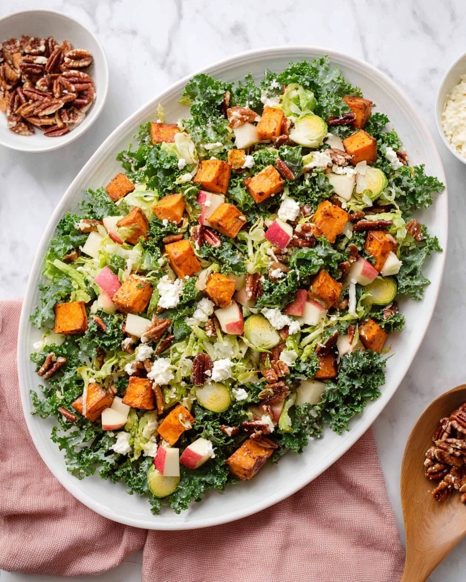 The image shows a white oval plate filled with a fresh salad. The base layer is made of curly dark green kale leaves, mixed with light green thin slices of Brussels sprouts and small red and white pieces of apple. Scattered on top are golden orange chunks of roasted sweet potato, creamy white crumbles of cheese, and dark brown toasted pecans that add texture. The salad is placed on a white marbled surface with a soft pink cloth partially visible on one side, and small white bowls containing extra pecans and cheese nearby. Photo taken with an iphone --ar 4:5 --v 7