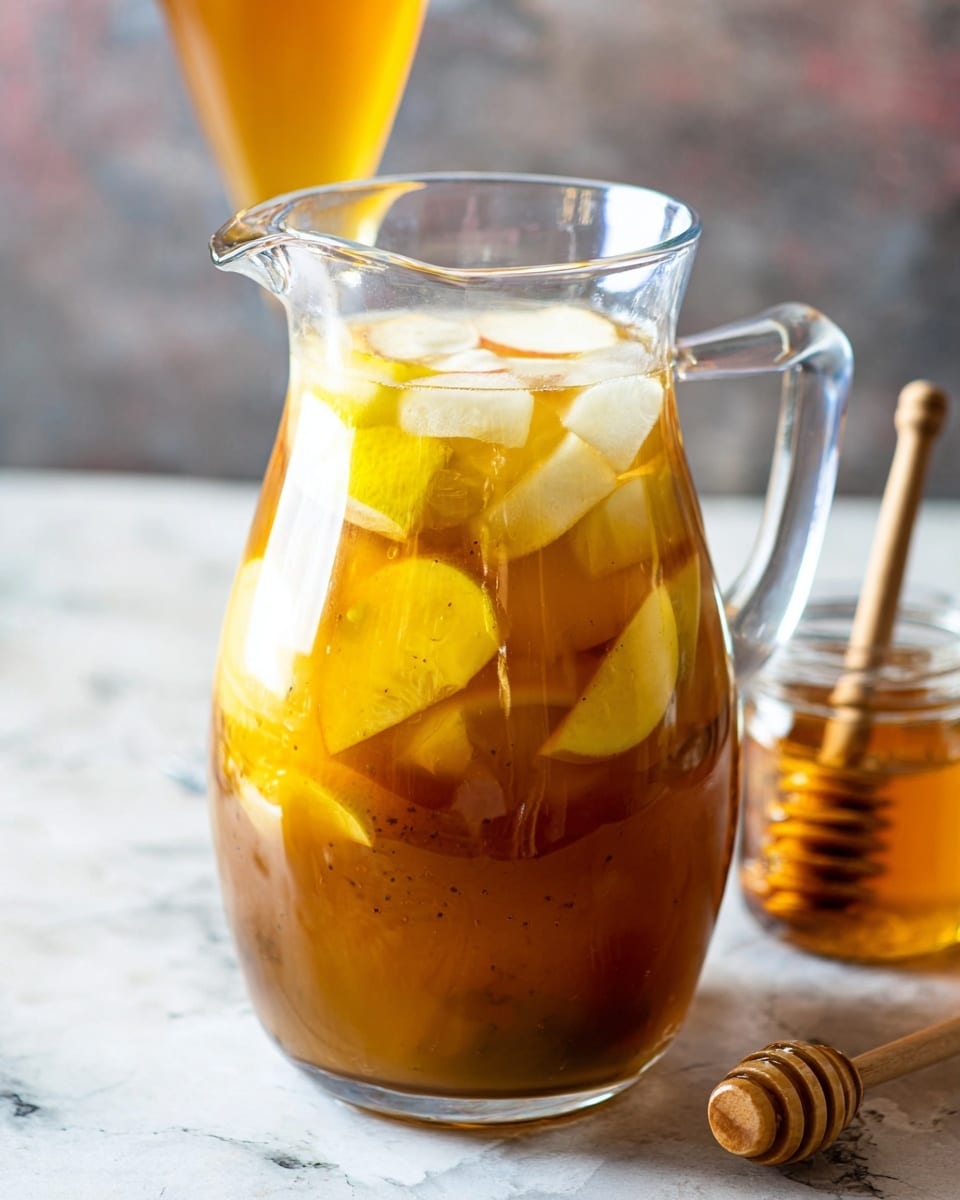 A clear glass pitcher filled with a golden-brown liquid, layered with slices of white and yellow fruit inside, creating a mix of smooth and slightly textured surfaces. The pitcher sits on a white marbled surface, and there is a small glass jar with honey and a wooden honey dipper resting inside it placed next to the pitcher on the right. In the blurred background, there is a tall clear glass with the same golden drink, showing a smooth texture. The lighting highlights the liquid's shine and the clarity of the glass, making the whole setup look fresh and inviting. photo taken with an iphone --ar 4:5 --v 7