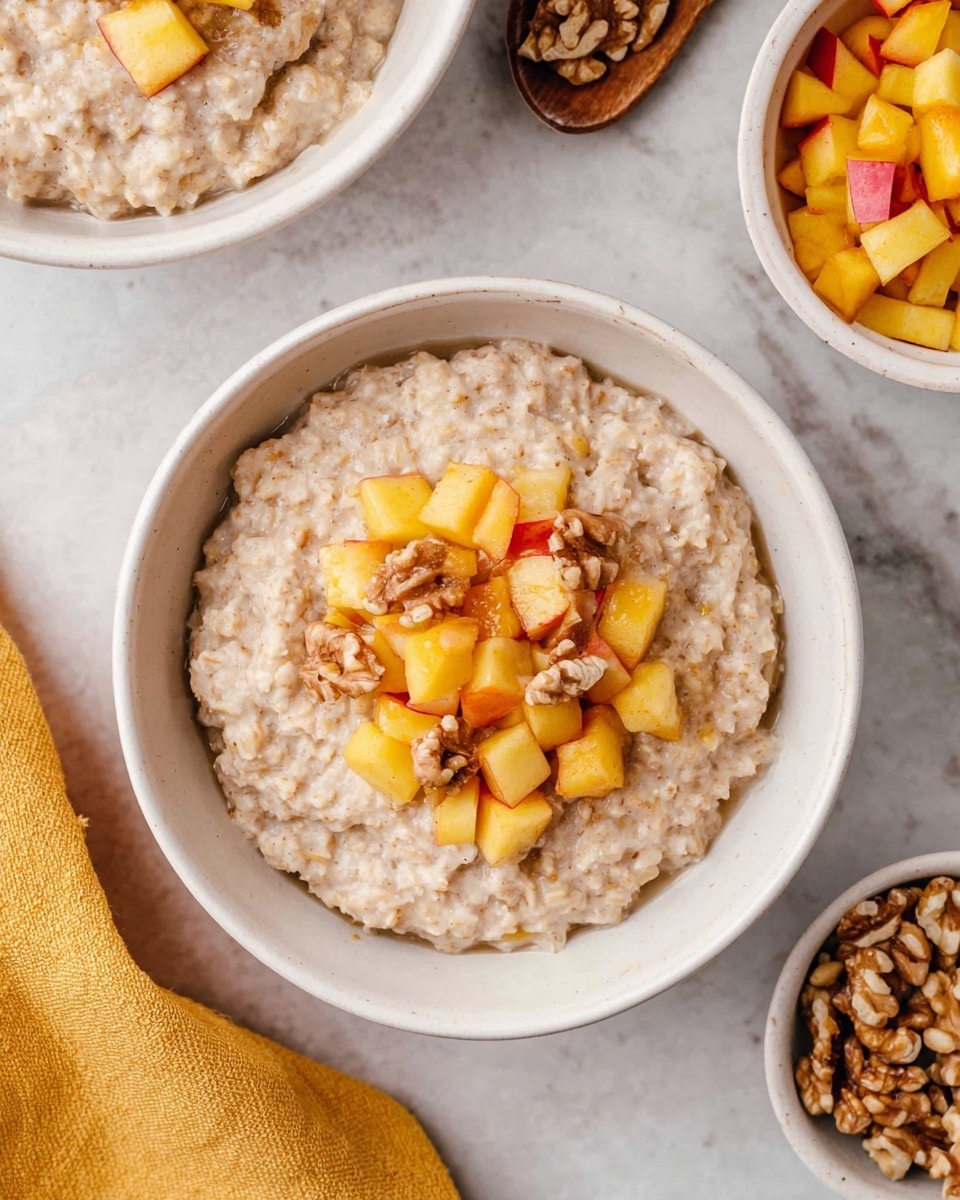 A white bowl filled with creamy oatmeal that has a soft, slightly bumpy texture, topped in the center with a layer of diced cooked apples showing warm orange and light red colors mixed with a few walnut pieces that are brown and slightly shiny. Another white bowl with more oatmeal is partially visible on a white marbled surface, along with a small white bowl of extra cooked apples to the side, and a small bowl with more walnuts nearby. A yellow cloth is placed near the bottom left corner of the image, and a woman’s hand is slightly visible reaching towards the bowl. photo taken with an iphone --ar 4:5 --v 7