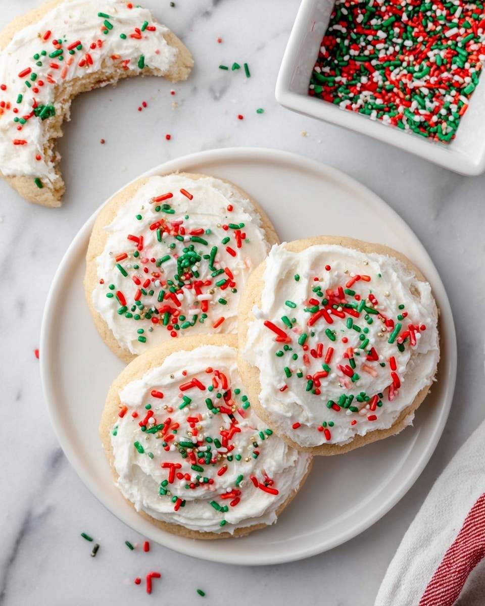 Three round cookies sit on a white plate placed on a white marbled surface, each cookie topped with a thick layer of creamy white frosting and sprinkled with red, green, and white jimmies. The cookies are light golden brown, soft in texture, and closely arranged on the plate, with one cookie slightly overlapping the other two. In the top right corner, a white square dish filled with the same colorful sprinkles rests on the surface, some sprinkles scattered around the plate and dish, adding a festive touch. A partially eaten cookie with white frosting and sprinkles is visible in the top left corner. Photo taken with an iphone --ar 4:5 --v 7