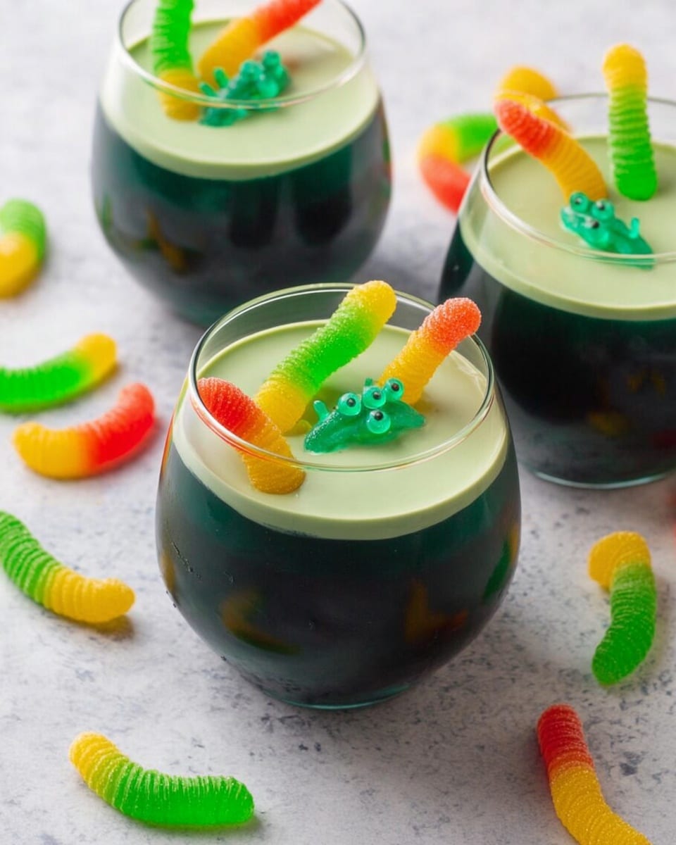 The image shows three clear round glasses filled with a dark green, smooth jelly-like layer that takes up about three-quarters of each glass. On top of this dark layer is a thick, light green creamy layer that covers the surface of the jelly. Each glass is decorated with colorful gummy worms and a small green gummy frog placed partly inside the creamy layer, with the worms sticking up in different directions. The glasses are placed on a white marbled surface, with a few more gummy worms and green frog gummies scattered around them. The look is playful and bright, with a mix of dark and light green colors and the bright colors of the candies adding fun details. photo taken with an iphone --ar 4:5 --v 7