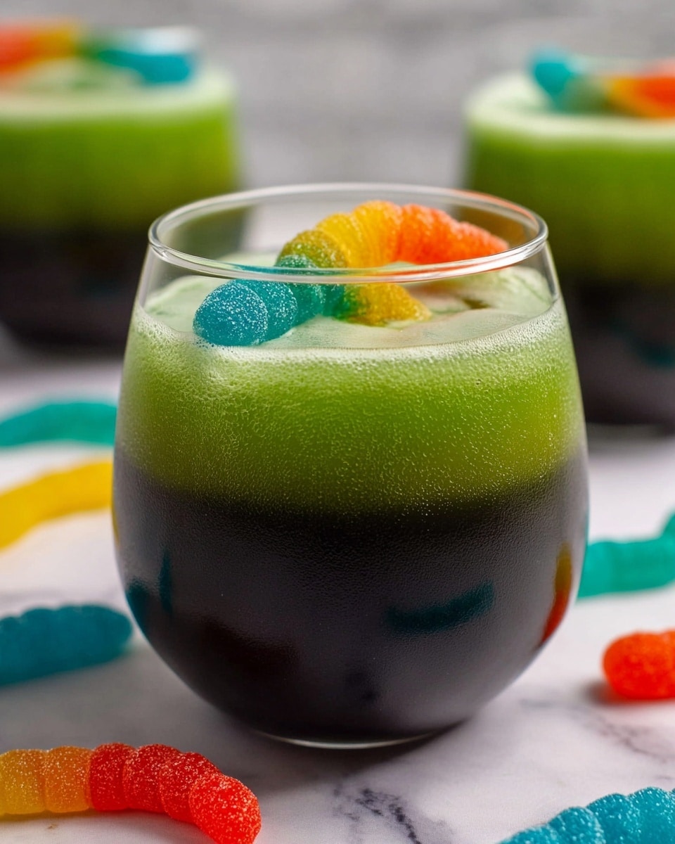 The image shows a close-up of a clear, round glass filled with three layers: the bottom layer is dark black and smooth, the middle layer is a wavy bright green, and the top layer is a light green foamy texture. On top, three colorful gummy worms stick out, one orange, one yellow-green, and one blue-red. The glass sits on a white marbled surface with more gummy worms scattered around and two more similar glasses blurred in the background. photo taken with an iphone --ar 4:5 --v 7