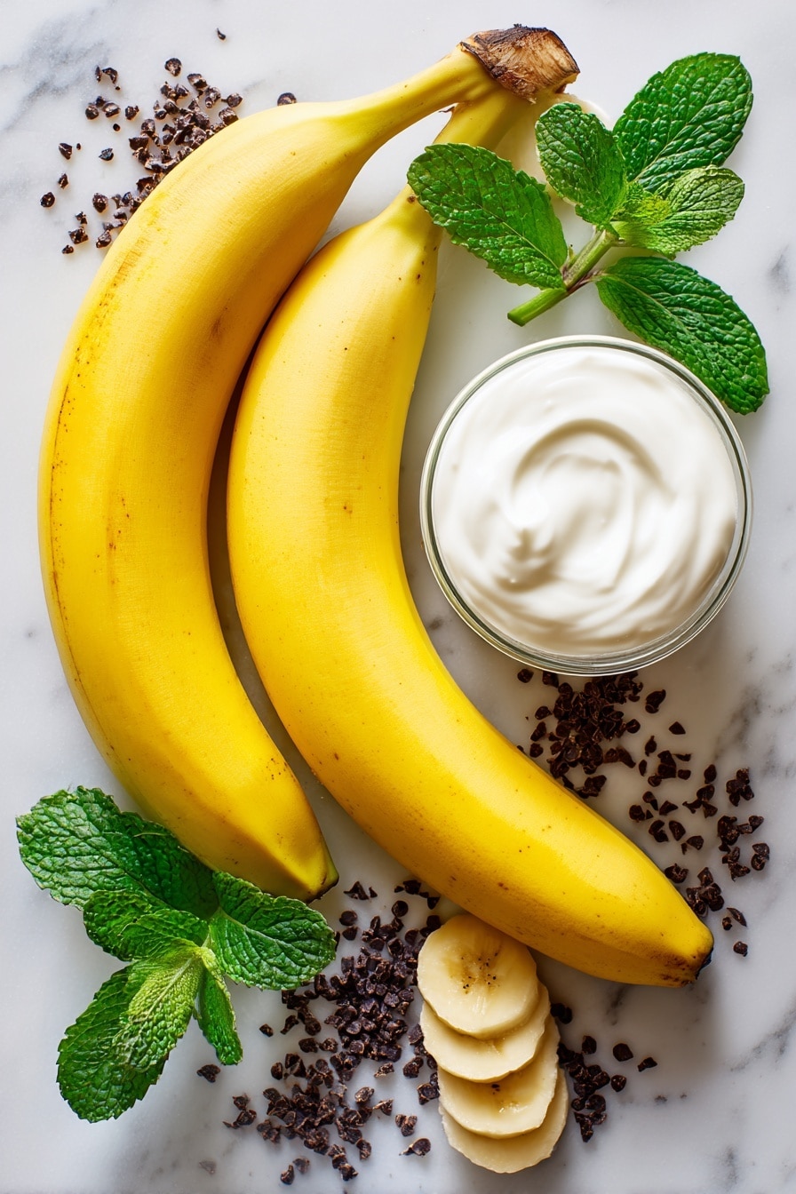 Boonanas, Halloween banana treats, frozen ghost snacks, healthy Halloween desserts, kid-friendly spooky snacks - Flat lay of two large ripe bananas with bright yellow skin, a small glass of smooth white vanilla yogurt, and scattered tiny dark mini chocolate chips with a glossy finish, all naturally arranged with a few banana slices showing their creamy texture, some fresh green mint leaves adding a pop of color, placed on white marbled surface, photo taken with an iphone --ar 2:3 --v 7