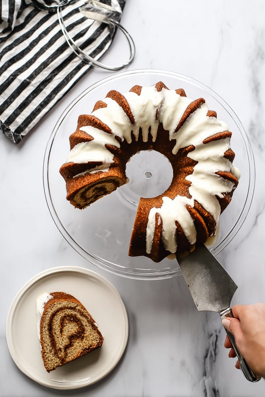 Cinnamon Bundt Cake with Cream Cheese Icing, cinnamon bundt cake, easy cinnamon cake recipe, soft cinnamon cake with icing, holiday bundt cake desserts - A bundt cake with a rich brown color and a thick white icing drizzled over the top that flows down the sides, leaving some of the cake visible between the icing sections. The cake is placed on a clear glass pedestal plate on a white marbled surface. One slice is cut out and placed on a white plate nearby, showing a swirl pattern inside with light and dark brown layers. A woman's hand is holding the cake server that has been used to lift the slice from the bundt cake. There is a striped black and white napkin to the side with a metal cake server on it. photo taken with an iphone --ar 2:3 --v 7