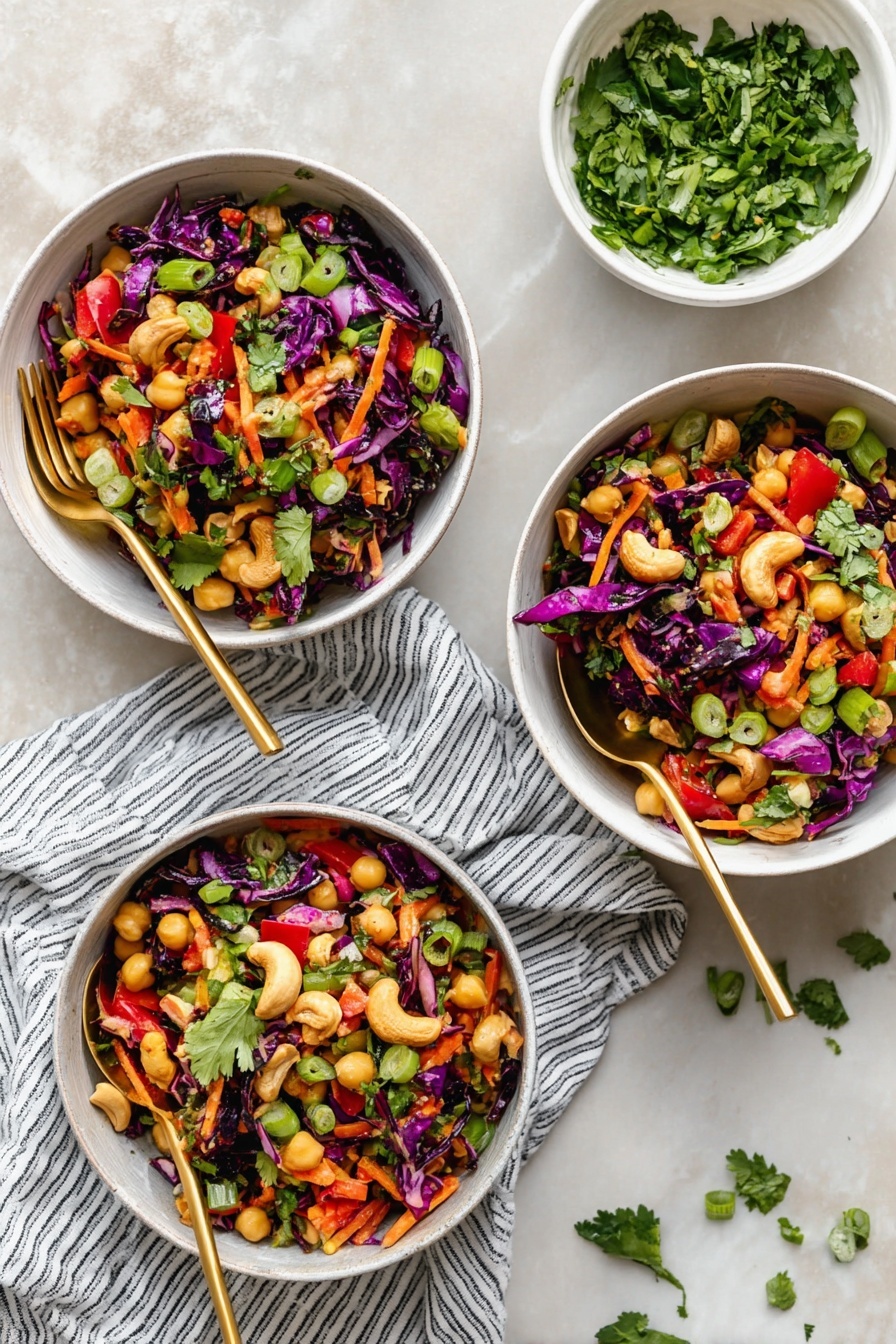 Chopped Thai-Inspired Chickpea Salad with Curry Peanut Dressing, Thai chickpea salad, healthy chickpea salad, Thai-inspired salads, vegan chickpea salad - Three white bowls filled with a colorful salad sit on a white marbled texture. Each bowl holds a mix of dark purple cabbage pieces, orange shredded carrots, light yellow chickpeas, green sliced scallions, red bell pepper chunks, and fresh green cilantro leaves scattered on top. There are some whole cashews on the salad adding a light beige color. Each bowl has a gold spoon resting inside, and a striped white and navy cloth lies underneath two of the bowls. A small white bowl with chopped cilantro sits above the bowls, with some cilantro leaves scattered on the surface. photo taken with an iphone --ar 2:3 --v 7