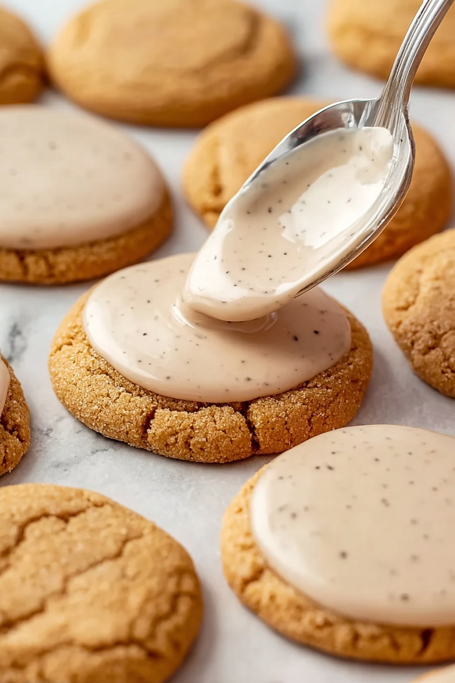 Brown Sugar Pop Tart Cookies, easy pop tart cookies, cinnamon glaze cookies, homemade sweet cookies, brown sugar dessert treats - Round light brown cookies with a soft, cracked surface are arranged on a white marbled background. A silver spoon is shown spreading a smooth, pale beige icing with small dark specks on the top surface of one cookie near the center. Several other cookies already have the same thin layer of icing evenly covering their tops while some remain plain. The cookies are placed closely together in rows and the icing appears glossy and creamy. Photo taken with an iphone --ar 2:3 --v 7