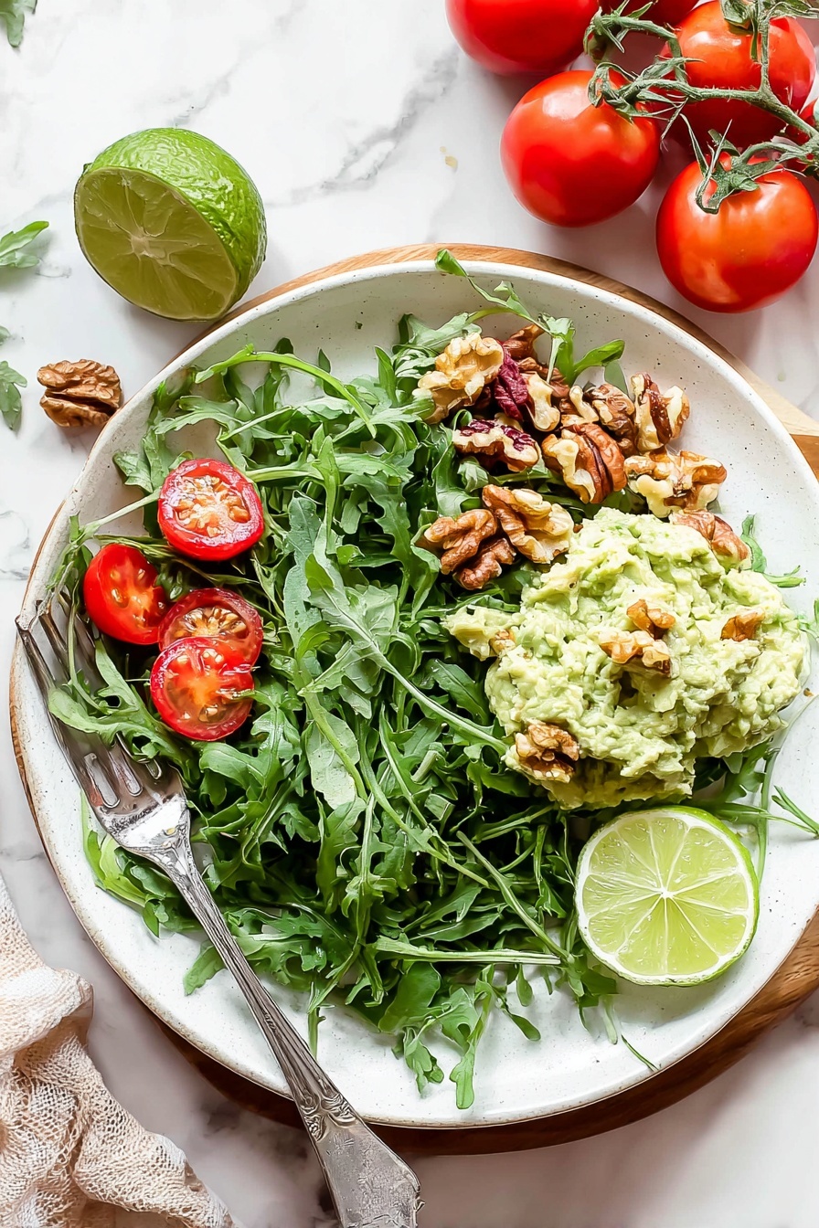 Healthy Greek Yogurt Avocado Chicken Salad, healthy chicken salad, Greek yogurt chicken salad, avocado chicken salad, quick healthy lunch - A white plate filled with a fresh salad on a white marbled surface. The bottom layer is a bed of dark green arugula leaves spread across the plate. Scattered on top are bright red cherry tomato halves and small brown walnut pieces. On one side, a creamy pale green mashed avocado mix is placed in a mound with a few walnut pieces on it. Two lime wedges, one light green and one yellow-green, rest on the mashed avocado. A silver fork is placed on the left side of the plate, partially resting on the salad. Nearby, whole red tomatoes on the vine and a halved lime sit on the white marbled background. Photo taken with an iphone --ar 2:3 --v 7