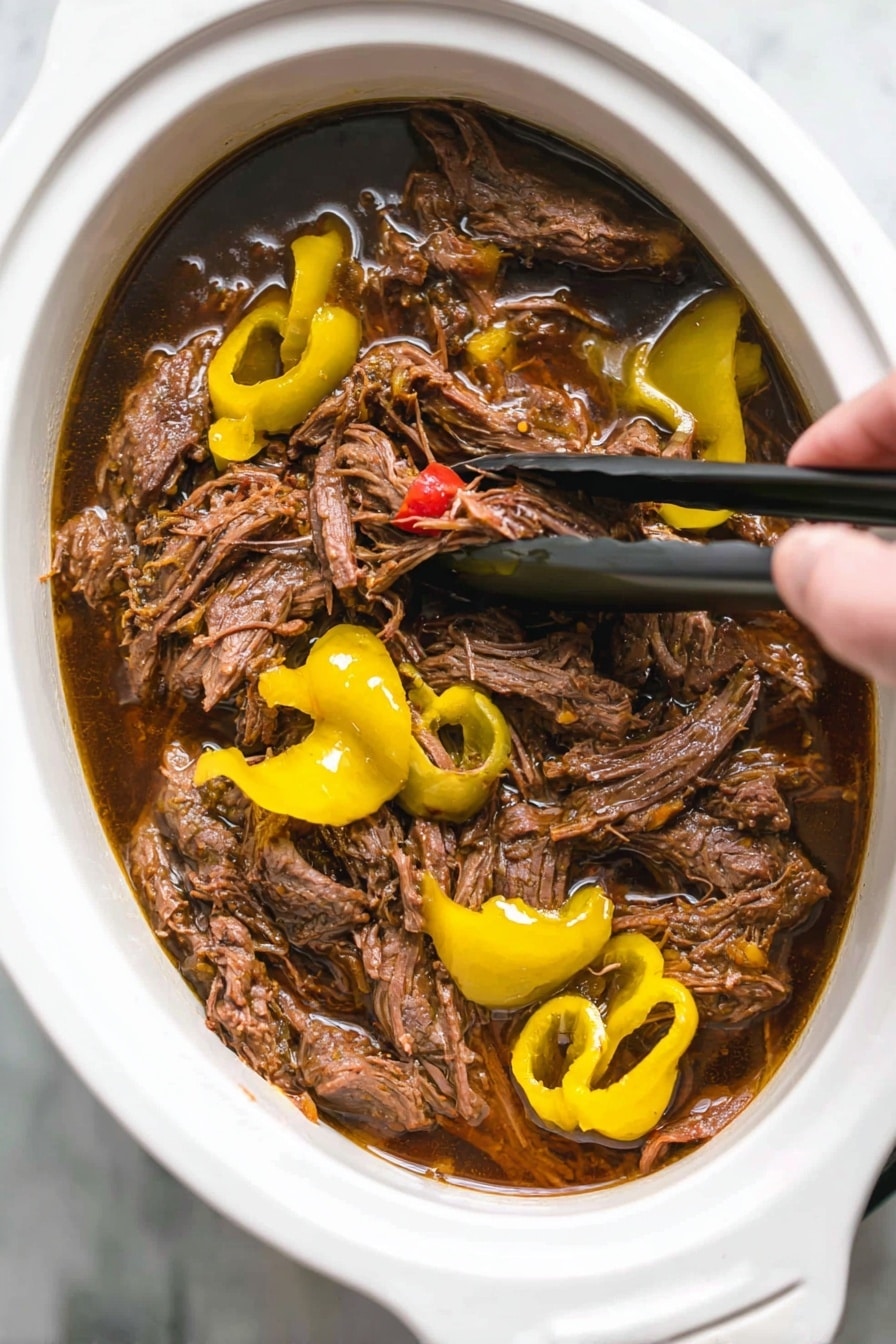 Italian Beef Sandwiches with Pepperoncini, Italian beef sandwiches, easy beef sandwich recipes, flavorful Italian sandwiches, hearty sandwiches with pepperoncini - A close-up shot of shredded brown meat soaked in dark brown juices inside a white oval slow cooker. The meat is mixed with bright yellow sliced peppers and whole pepper shapes on top. Woman's hand is visible holding black tongs, lifting some meat from the cooker. The background surface is white marble. photo taken with an iphone --ar 2:3 --v 7