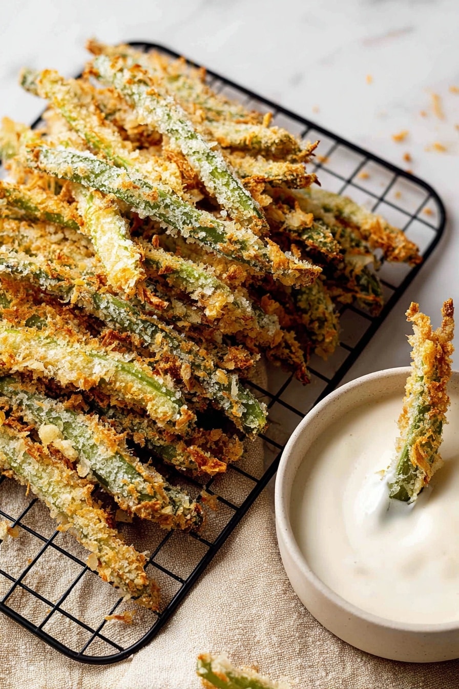 Green Bean Fries, healthy vegetable snacks, crispy green bean bites, easy veggie side dishes, baked green bean snacks - The image shows many breaded green beans stacked on a black wire cooling rack on a white marbled surface with a beige cloth underneath. The beans have a crunchy, golden-brown coating with bits of light and darker browns and the green of the beans is visible under the crumbs. To the right, there is a white bowl filled with thick, creamy white dip, with two breaded green beans dipped into it. The texture of the dip is smooth and slightly shiny. Photo taken with an iphone --ar 2:3 --v 7