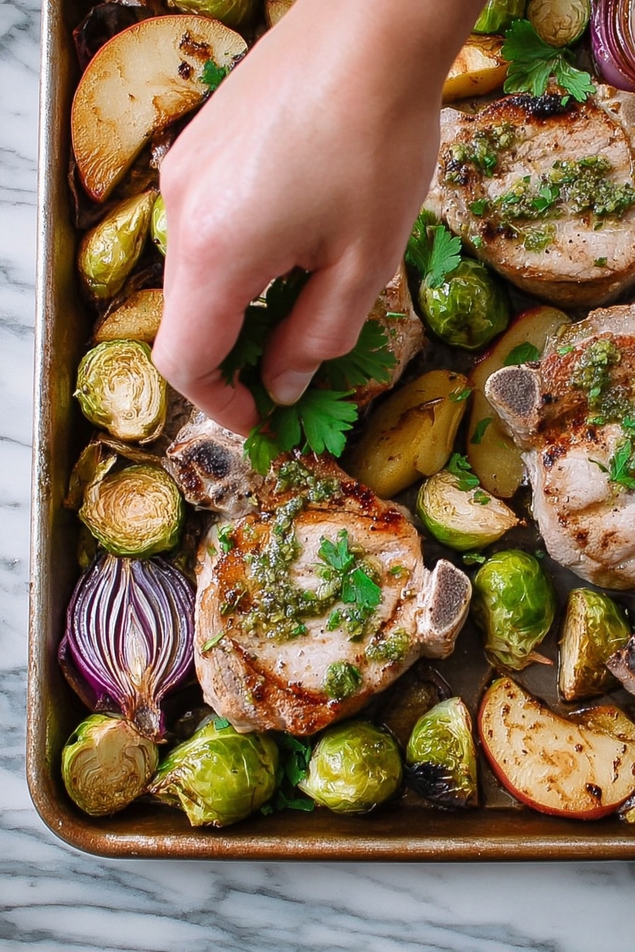 Sheet Pan Pork Chop Supper with Apples, Brussels Sprouts, and Sage, one-pan pork chop dinner, easy sheet pan pork recipes, healthy pork chop meals, flavorful apple and Brussels sprouts dinner - A close-up view of a metal tray filled with cooked pork chops and roasted vegetables. There are three pork chops, each light brown with grill marks and green herb sauce on top, scattered across the tray. Around the pork chops, there are halved Brussels sprouts with a charred, darker green color, quartered pieces of red onions with purple layers, and golden brown apple slices. A woman's hand is gently placing fresh green parsley leaves over the pork chops. The tray sits on a white marbled surface. photo taken with an iphone --ar 2:3 --v 7