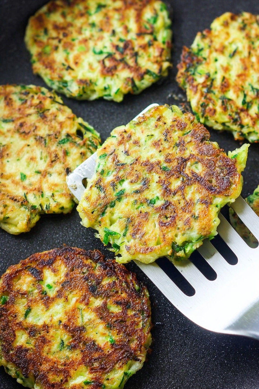 Vegan Zucchini Fritters, vegan zucchini fritters, crispy zucchini patties, healthy zucchini snacks, plant-based fritters - There are several flat, round fritters cooking on a black pan. Each fritter shows a mix of green herbs and light yellow batter, with crisp, dark brown patches where they have browned. One fritter is lifted by a silver spatula with long slots, showing its uneven edges and slightly rough texture. The overall look is crispy and fresh, with the green and yellow colors standing out against the pan. photo taken with an iphone --ar 2:3 --v 7
