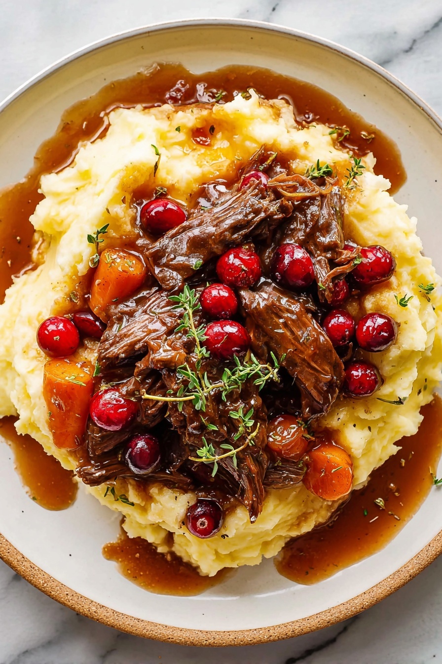 Cranberry Balsamic Roast Beef, Roast Beef with Cranberries and Balsamic, Holiday Roast Beef Recipes, Tender Slow-Cooked Beef with Cranberries, Unique Roast Beef Ideas - A white plate holds a large bed of soft, creamy mashed potatoes that have a smooth, slightly lumpy texture and a pale yellow color. On top, there are several pieces of dark brown shredded beef covered in a glossy, thick brown gravy with visible chunks of carrots, pearl onions, and whole bright red cranberries scattered throughout. Fresh small green herb leaves, possibly thyme, are sprinkled over the dish. Some gravy has spilled onto the plate, adding a rich shine. The plate sits on a white marbled surface. Photo taken with an iphone --ar 2:3 --v 7