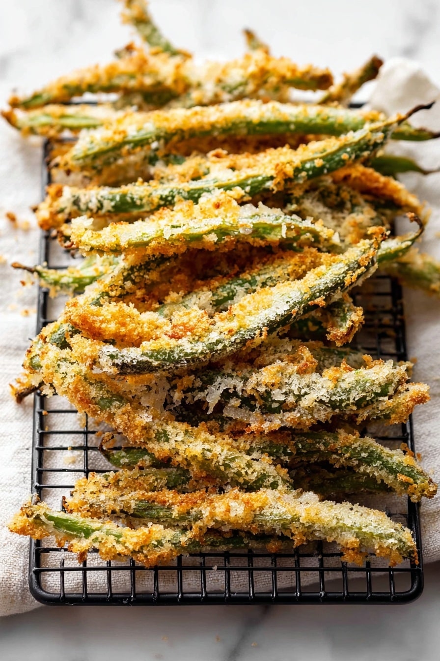 Green Bean Fries, healthy vegetable snacks, crispy green bean bites, easy veggie side dishes, baked green bean snacks - The image shows a stack of crispy baked green beans coated with a light golden-brown breadcrumb crust. The green beans are arranged in a slightly overlapping pile on a black wire rack that sits on top of a white marbled surface with a soft white cloth underneath. The crumb coating is uneven with some areas showing more toasted crispiness and a mix of pale and deeper golden colors. The green beans are long and thin, with their stems visible at the edges, and the texture looks crunchy and rustic. photo taken with an iphone --ar 2:3 --v 7