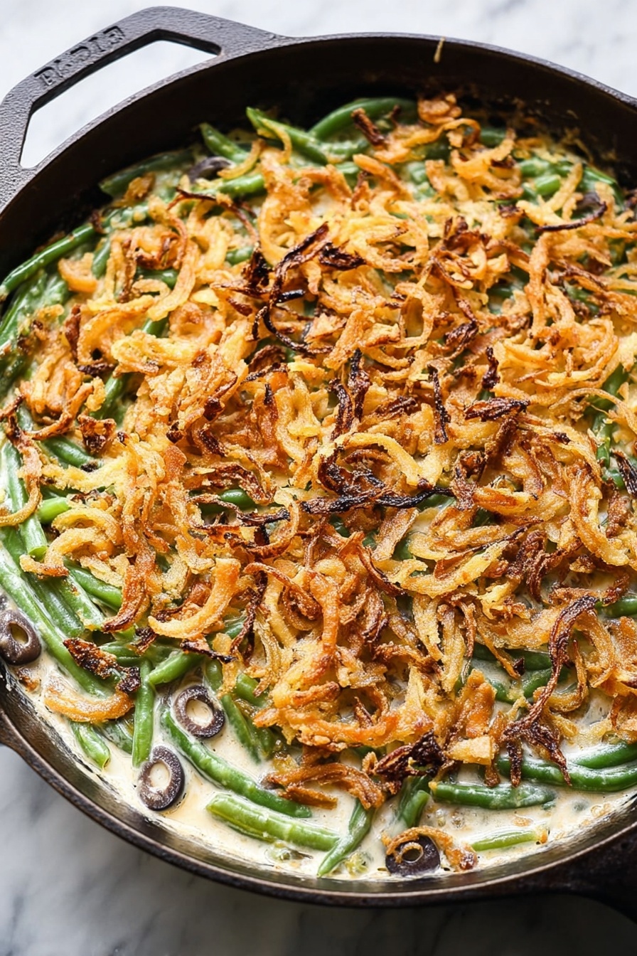 Vegan Green Bean Casserole, plant-based holiday casserole, vegan green bean dish, dairy-free green bean casserole, healthy vegan green bean recipe - This image shows a close-up of a baked green bean casserole in a cast iron pan placed on a white marbled surface. The bottom layer consists of bright green beans mixed with sliced black olives visible within a creamy, white sauce. On top of this, there is a thick, even layer of crispy, golden-brown fried onion strips spread across the entire pan, giving the dish texture and a crunchy appearance. Some onion strips have darker, almost burnt edges which add color contrast. The round pan's black handle is partly visible, framing the dish. Photo taken with an iphone --ar 2:3 --v 7