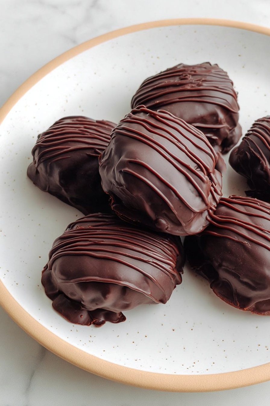 Raspberry Date Brownie Bites, healthy brownie snacks, no-bake energy bites, gluten-free brownie treats, wholesome dessert ideas - The image shows a white plate with a few pieces of chocolate-covered treats. Each treat is covered in a smooth, dark chocolate layer with some thin, wavy lines of chocolate drizzled on top for decoration. The chocolate coating looks thick and glossy, and the treats have rounded, uneven shapes. The plate has small speckles on it and sits on a white marbled surface. photo taken with an iphone --ar 2:3 --v 7