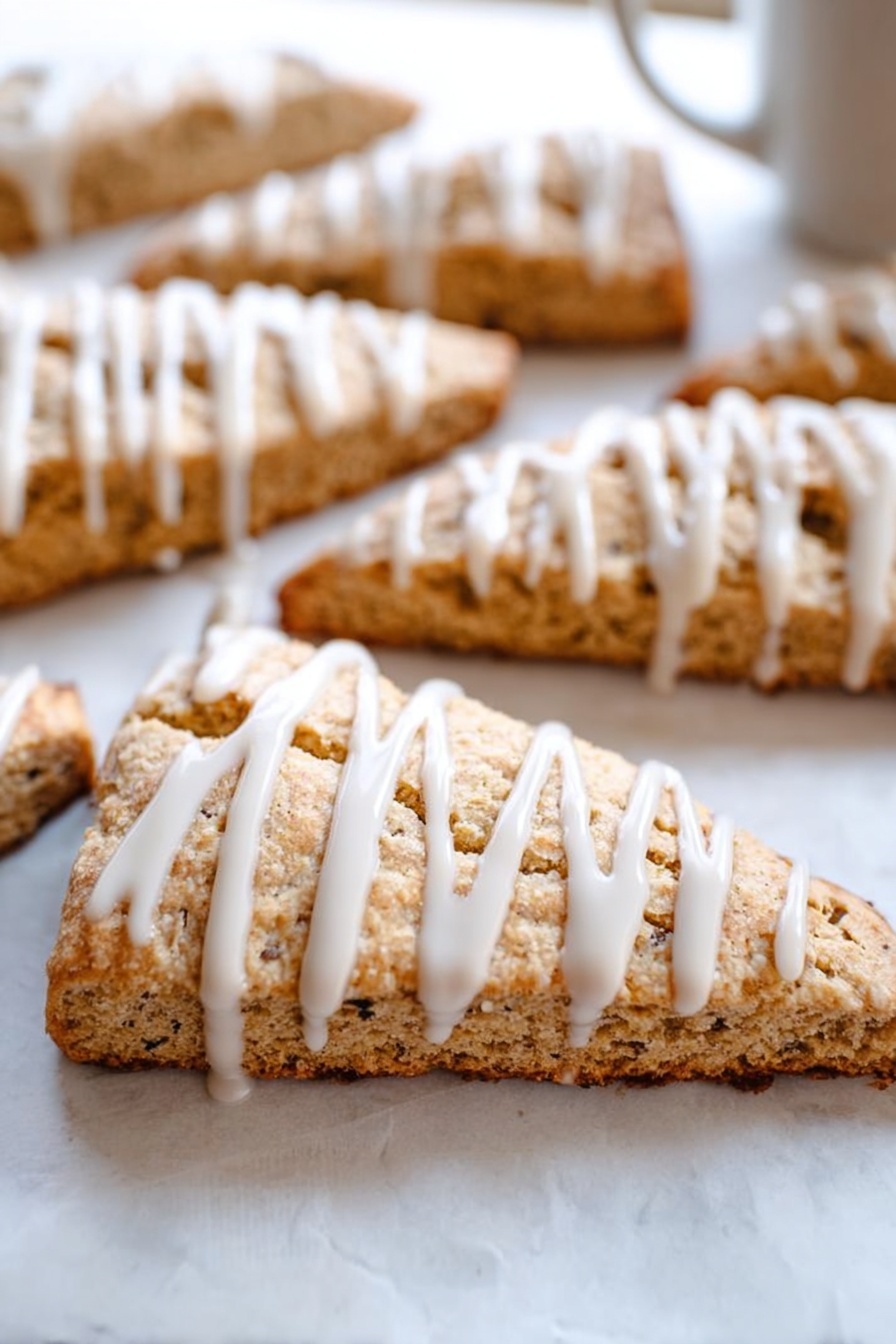 Cinnamon Vanilla Biscotti, biscotti recipe with cinnamon vanilla, how to make cinnamon vanilla biscotti, crunchy biscotti with vanilla and cinnamon, homemade cinnamon vanilla biscotti - This image shows several triangular slices of light brown scones arranged on white parchment paper over a white marbled surface. Each scone slice has a visible crumbly texture with small dark specks inside. On top of each slice, there is a thick white icing drizzle applied in vertical lines, adding contrast and a smooth, glossy look to the rough texture of the scones. The focus is on a front scone slice, with others blurred in the background, giving depth to the image. photo taken with an iphone --ar 2:3 --v 7