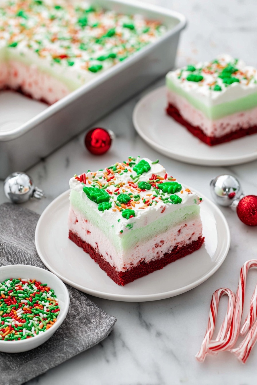 Festive Red Velvet Christmas Dessert, holiday dessert, Christmas cake, red velvet holiday treat, festive layered dessert - The image shows a festive layered dessert square on a white plate, placed on a white marbled surface. The dessert has four distinct layers: the bottom layer is a dense dark red cake, followed by a light pink creamy layer with red specks, then a smooth pale green gelatin layer, and finally topped with a thick white whipped cream layer decorated with green, red, orange, and white sprinkles shaped like leaves, dots, and sticks. In the background, there is a silver baking pan with a large portion of the same dessert topped with sprinkles, and another smaller white plate holds a similarly decorated dessert square. Nearby, a small white bowl filled with matching festive green and red sprinkles sits next to two small candy canes, a silver ornament ball, a red ornament ball, and a gray cloth napkin. Photo taken with an iphone --ar 2:3 --v 7
