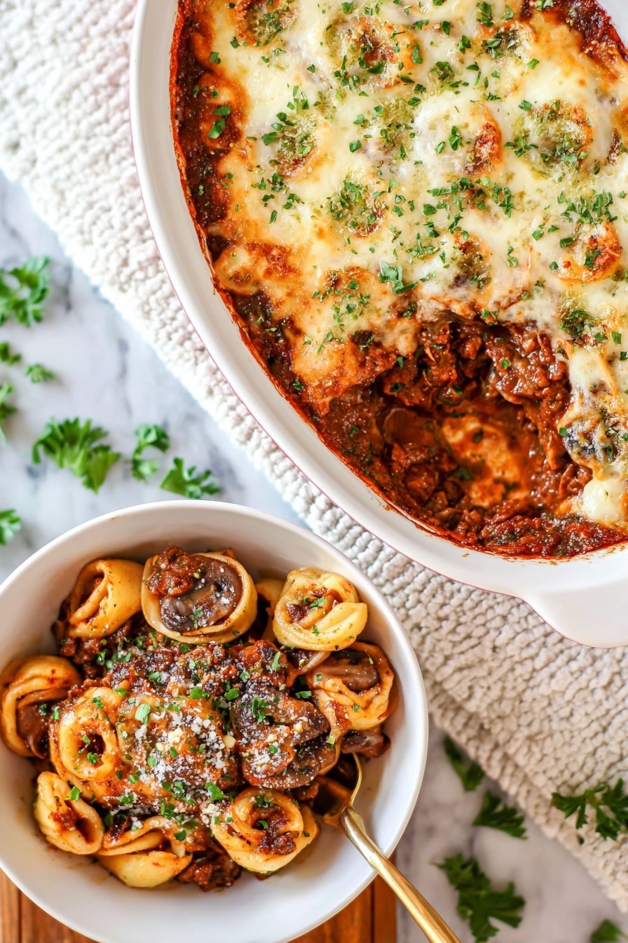 Cheesy Baked Tortellini with Beef, cheesy baked tortellini, beef tortellini casserole, hearty tortellini pasta bake, easy cheese tortellini dish - The image shows a white oval baking dish with a layered casserole on a white marbled surface. The top layer is melted, lightly browned cheese sprinkled with green herbs. A section is scooped out, revealing a rich, dark brown meat sauce mixed with whole mushrooms and tortillas shaped like small circles inside the dish. Next to it is a white bowl filled with a serving of the casserole, showing layers of browned meat sauce, mushrooms, and pasta circles, all topped with some grated cheese and chopped green herbs. A golden spoon is partially visible in the bowl. The background includes a white textured cloth and scattered green herb leaves. photo taken with an iphone --ar 2:3 --v 7