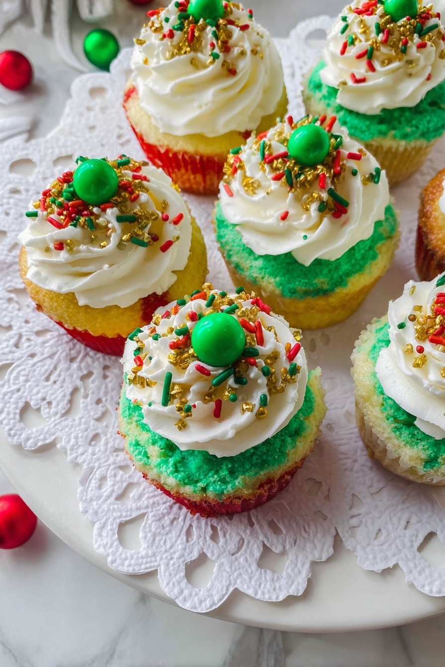 Mini Christmas Cheesecake Bites, Christmas Cheesecake Bites, holiday cheesecake treats, festive mini cheesecakes, easy Christmas dessert - The image shows six cupcakes placed on a white plate covered with a white paper doily. Each cupcake has three visible layers of cake with red, yellow, and green colors, stacked one on top of another. On top of the cake layers is a thick layer of green frosting spread evenly. Over this green frosting, there is a generous swirl of white whipped cream. The whipped cream is decorated with holiday-themed sprinkles in red, green, and gold, including small rods, round dots, and tiny gold balls. Two cupcakes have a green candy ball placed in the center on top of the whipped cream. The plate is set on a white marbled surface with some colorful decorations partially visible around the edges. photo taken with an iphone --ar 2:3 --v 7