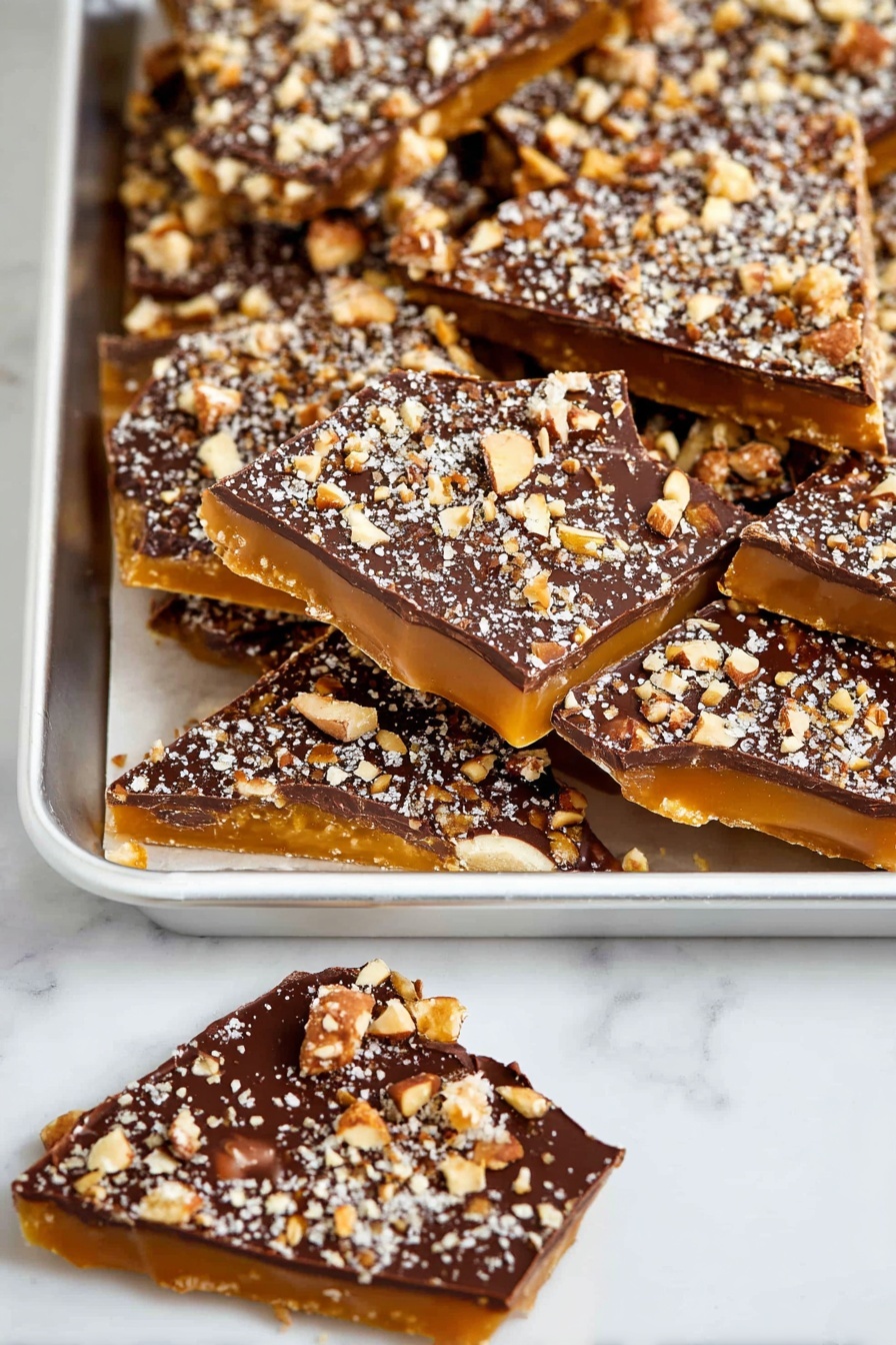 Homemade Toffee with Chocolate and Pecans, decadent chocolate pecan toffee, easy homemade candy, buttery toffee recipe, crispy chocolate topping - The image shows a white tray full of irregular triangular pieces of candy with three visible layers: a bottom layer of golden caramel, a shiny middle layer of smooth dark chocolate, and a top layer sprinkled heavily with crushed nuts in light brown and white tones. Next to the tray are two more pieces of the same candy, one fully visible and one partly shown, lying on a white marbled surface. The overall look is rich and textured with the nut pieces creating a rough surface on top of the smooth chocolate layer photo taken with an iphone --ar 2:3 --v 7