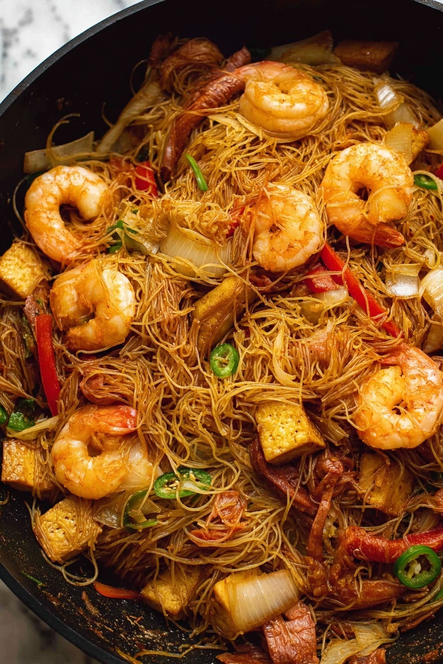 Singapore Noodles with Shrimp and Curry, Singapore Noodles recipe, shrimp noodle stir-fry, spicy curry noodles, quick Asian noodle dish - A black pan filled with stir-fried thin noodles mixed with large cooked shrimp that are a light orange color with a slightly shiny texture. There are pieces of sliced red bell pepper and green chili scattered throughout the noodles, along with chunks of browned tofu that have a slightly crispy outside. Thin slices of cooked brown meat and translucent, soft-looking onion slices are also mixed in. The noodles are tangled and lightly coated in a soy-colored sauce. The background is a white marbled texture. photo taken with an iphone --ar 2:3 --v 7