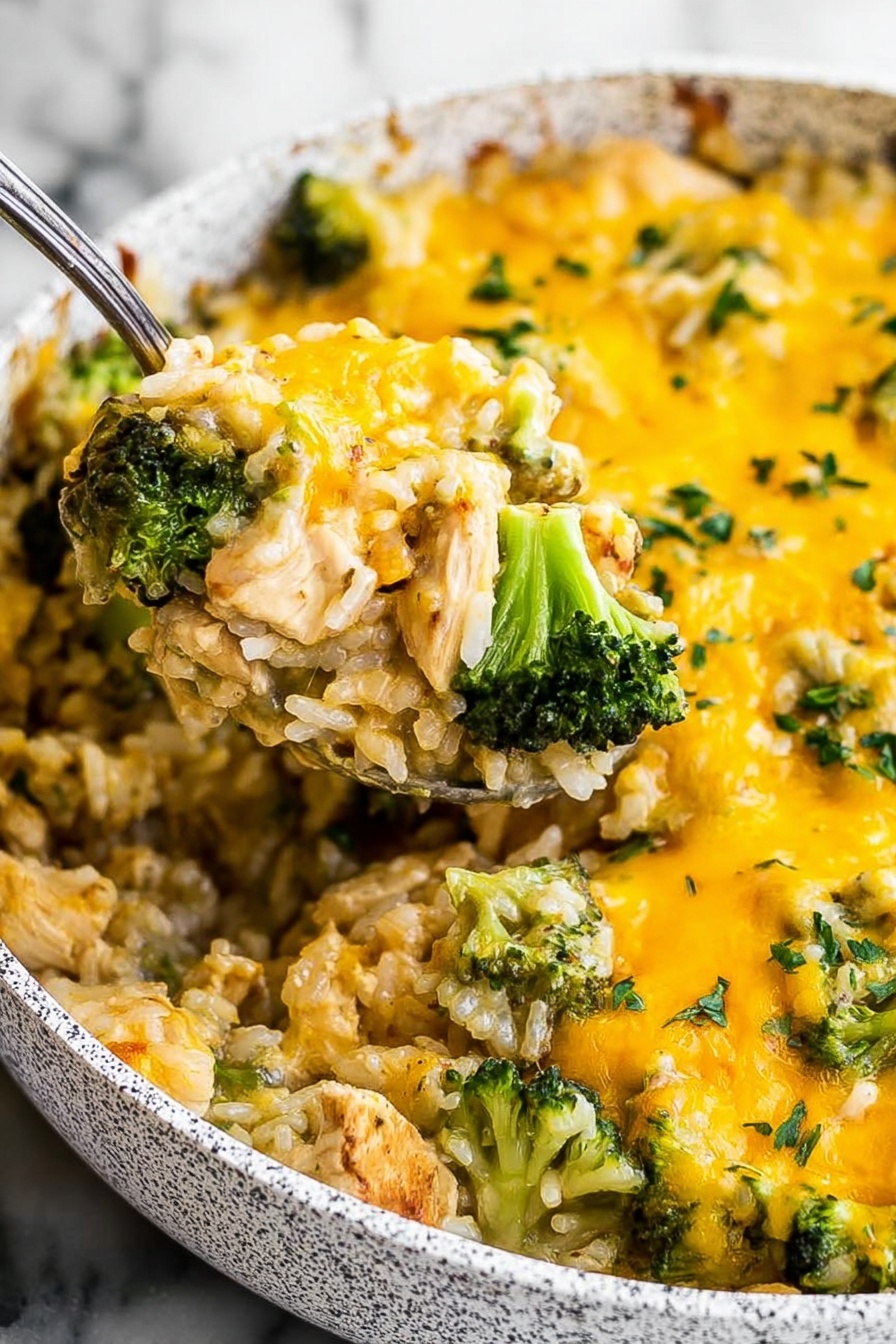 Cheesy Chicken Broccoli Rice Bake, easy chicken casserole, creamy broccoli rice bake, weeknight comfort food, 30-minute dinner - The image shows a close-up of a dish in a white speckled pan filled with a cheesy mixture. The dish has two main layers: at the bottom, tender pieces of light brown chicken mixed with white rice; on top, bright green broccoli florets are scattered evenly. A thick layer of melted yellow cheese covers the whole dish, with some green herbs sprinkled on top. A metal spoon lifts a portion, showing the mix of chicken, rice, broccoli, and cheese together. The background is a white marbled texture. Photo taken with an iphone --ar 2:3 --v 7