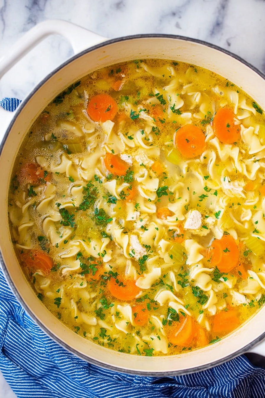 Vegan Chicken Noodle Soup, plant-based chicken noodle soup, hearty vegan soup recipes, vegan comfort food, easy vegan noodle soup - A white pot filled with clear yellow broth soup containing wavy egg noodles that float through the liquid. Slices of bright orange carrots and pale green celery are mixed evenly throughout the soup, along with small pieces of white chicken. The soup is topped with finely chopped fresh green herbs, adding small bursts of color. The pot is resting on a white marbled surface next to a blue striped cloth. Photo taken with an iphone --ar 2:3 --v 7