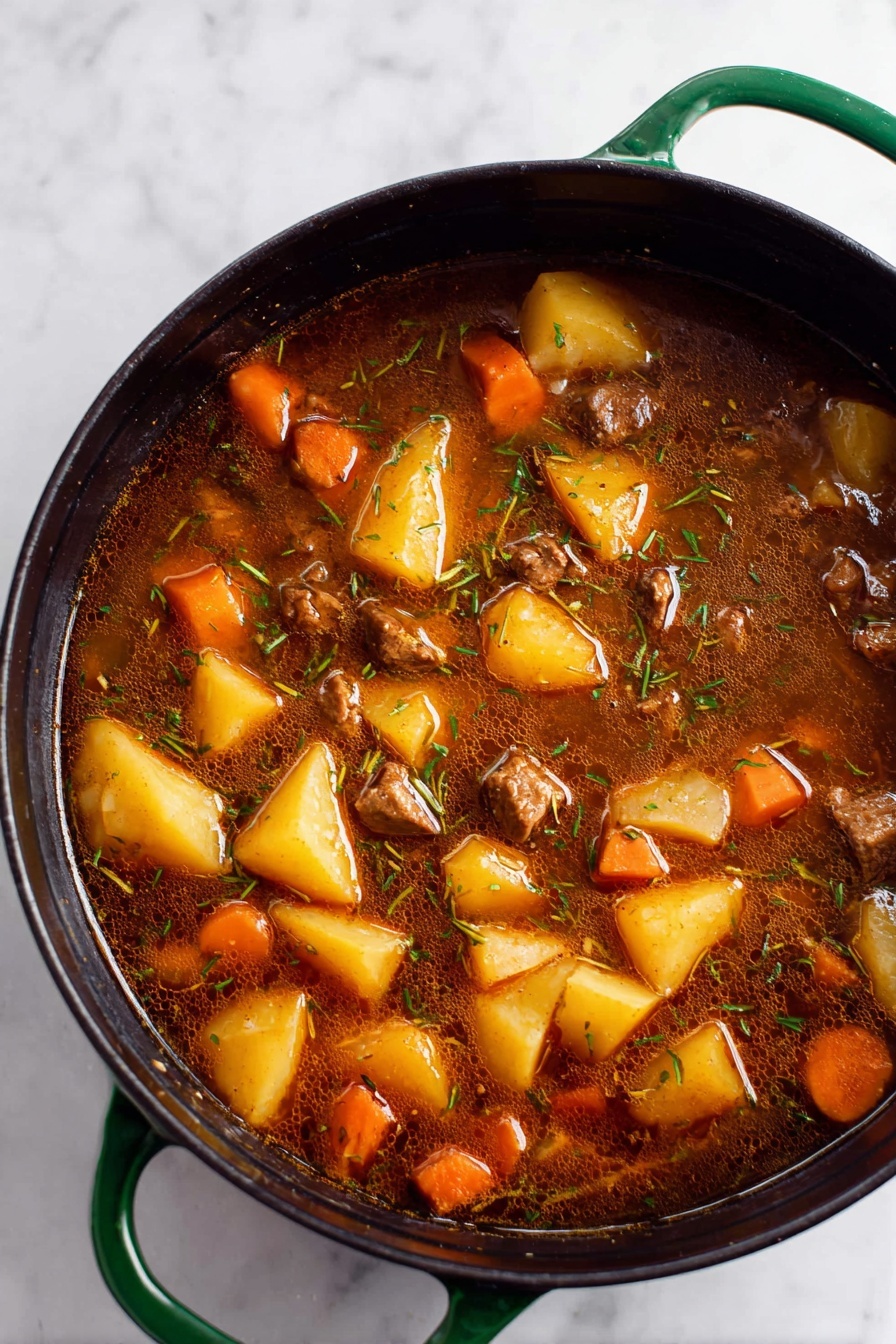 Vegan Irish Stew with Beer, Irish vegan stew, plant-based Irish stew, hearty vegan stew, vegan Guinness stew - A close-up top view of a large black pot with green handles filled with a rich brown stew. The stew has large chunks of yellow potatoes, orange carrot pieces, and small cubes of brown meat mixed evenly throughout. The broth is dark, slightly oily, with visible thin strands of herbs floating on the surface. The pot sits on a white marbled surface. photo taken with an iphone --ar 2:3 --v 7