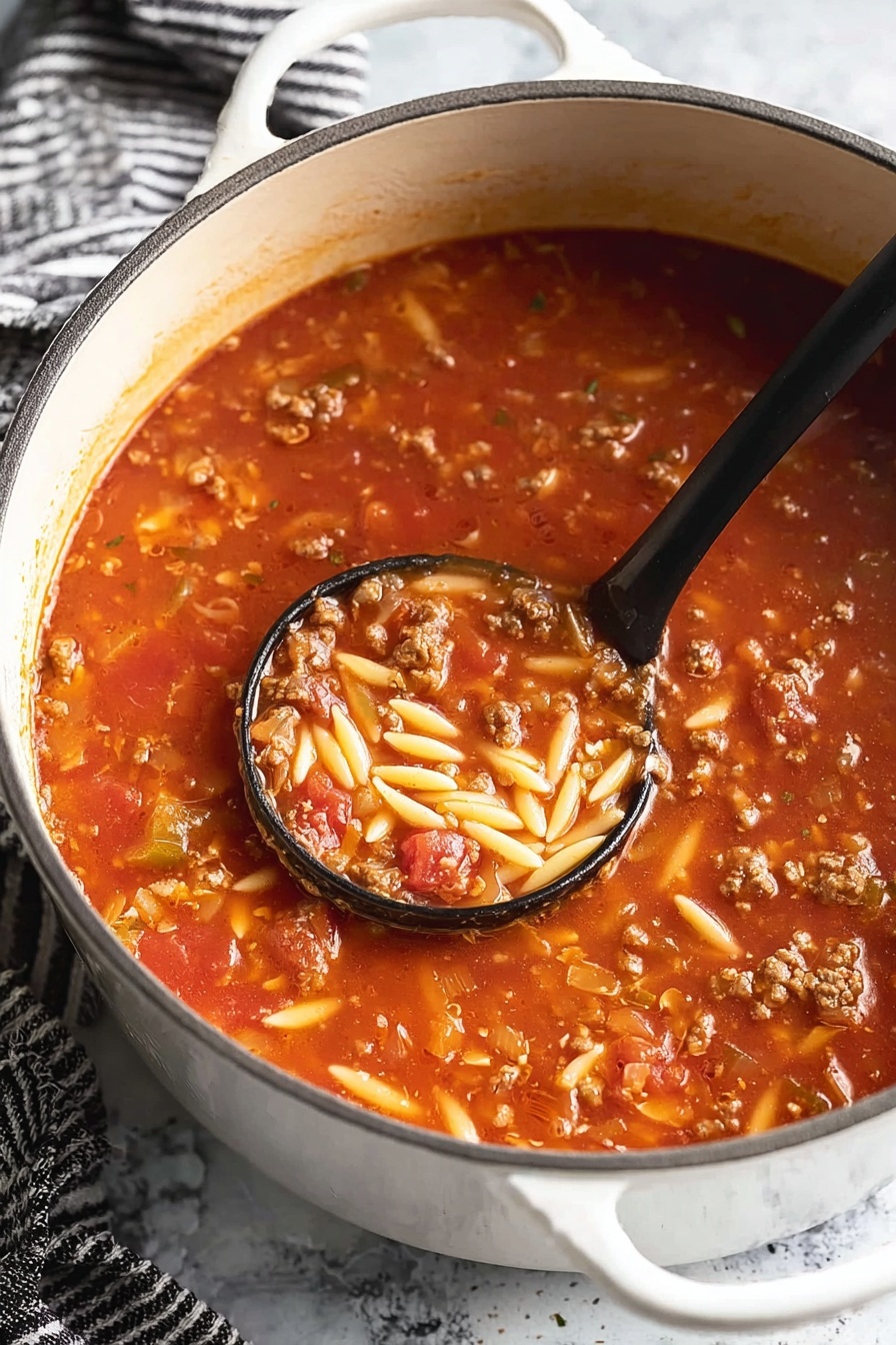 Italian Sausage and Orzo Soup, Italian sausage and orzo soup, hearty Italian sausage soup, easy Italian sausage soup, comforting soup recipes - A white pot filled with a thick tomato soup that has three visible layers: a bright red tomato base with a smooth texture, mixed with small chunks of cooked ground meat in brown color, and short, oval-shaped pieces of light yellow pasta scattered throughout. A black ladle scoops some soup near the center, showing all three layers together with a shiny, moist texture. The pot is on a white marbled surface with a black-and-white striped cloth nearby. Photo taken with an iphone --ar 2:3 --v 7
