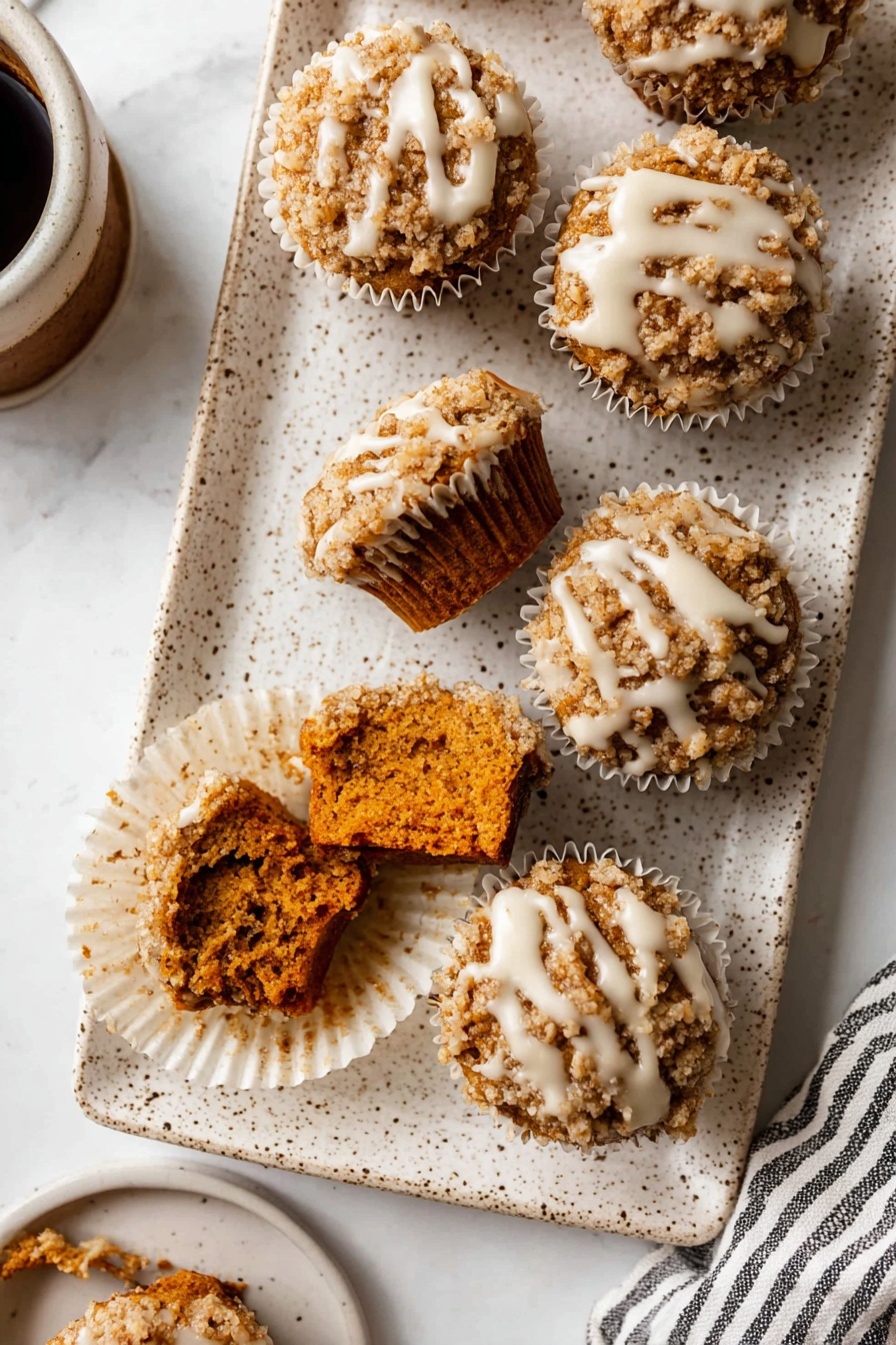 Pumpkin Crumb Muffins with Maple Icing, Pumpkin Muffins, Fall Muffin Recipes, Moist Pumpkin Muffins, Easy Pumpkin Muffin Recipe - The image shows a white speckled rectangular plate holding seven small muffins with crumbly tops. Each muffin has a rough, light brown crumb layer with a drizzle of white icing over it. Two muffins in the front have bites taken out, showing a dense, dark orange interior. The muffins sit inside white paper liners arranged close to each other. The plate is on a white marbled textured surface with part of a cup of coffee and a striped cloth visible on the edges. photo taken with an iphone --ar 2:3 --v 7