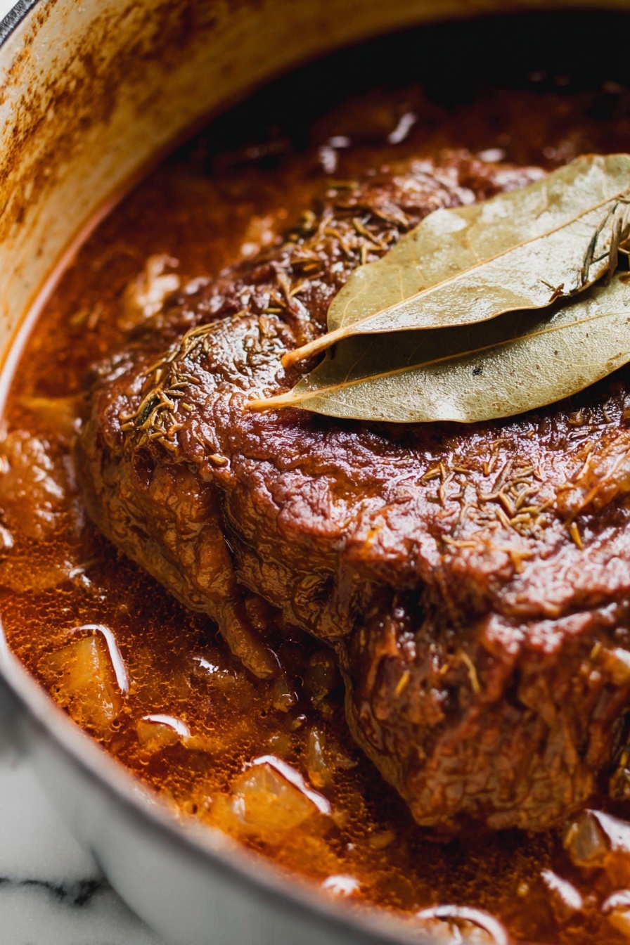 French Onion Pot Roast, French Onion Soup Pot Roast, savory pot roast with caramelized onions, easy French onion pot roast, comforting meat recipes - The image shows a close-up of a rich, dark brown meat stew in a pot, with the main piece of meat at the center, covered in thick sauce. The meat has a textured surface with visible herbs and spices, and it looks tender and juicy. Two dry, light brown bay leaves rest on top of the meat, adding a layer of texture and color contrast. The stew sauce has a glossy finish with chunks visible around the edges, and the pot’s inner side is stained in a brownish color from the cooking. The background is a white marbled texture. photo taken with an iphone --ar 2:3 --v 7