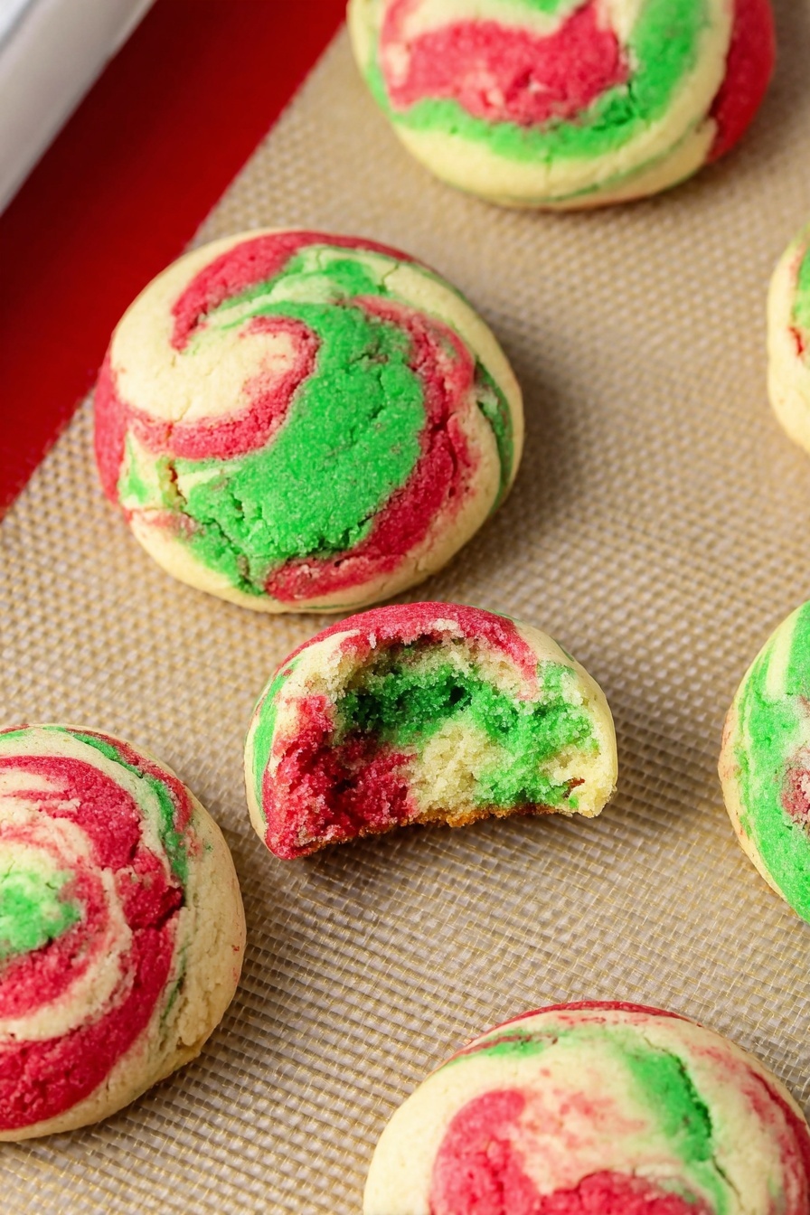 Peppermint Cheesecake Cookies, festive peppermint cookies, holiday cheesecake cookies, peppermint dessert recipes, soft peppermint cookies - This image shows a baking tray lined with a beige silicone mat that holds eight round cookie dough balls. Each ball has three swirled colors: green, red, and white, giving a marbled effect. The dough balls are spaced evenly, with a slightly rough texture on top and smooth sides. The tray has a silver metal edge and a red silicone border around the baking mat. The background is a white marbled texture. photo taken with an iphone --ar 2:3 --v 7