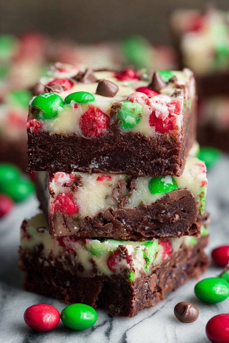 Christmas Brownie Bars with M&Ms, festive brownie bars, holiday chocolate dessert, easy Christmas brownie recipe, M&Ms brownie treats - The image shows a close-up of three stacked dessert bars with two clear layers. The bottom layer is thick, dense, and dark brown with a fudgy texture. The top layer is thinner and creamy white, embedded with red and green candy pieces and small chocolate chunks scattered throughout. Around the stack, several red and green round candies with a shiny shell are scattered. The background has a white marbled texture. photo taken with an iphone --ar 2:3 --v 7
