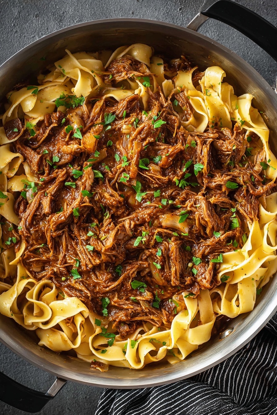 Short Rib Ragu, short rib ragu recipe, hearty beef ragu, slow-cooker ragu, Italian beef stew - The image shows a close-up of a pan filled with two main layers: the bottom layer is flat, wide pasta noodles in a pale yellow color, and the top layer is shredded meat cooked in a rich brown sauce. The shredded meat is mixed with small, finely chopped green herbs scattered evenly over the dish, adding spots of bright green color. The pan is metallic and round, resting on a dark gray surface with a striped black and white cloth visible at the bottom right. The overall look is hearty and rustic with a mix of smooth noodles and textured meat. photo taken with an iphone --ar 2:3 --v 7