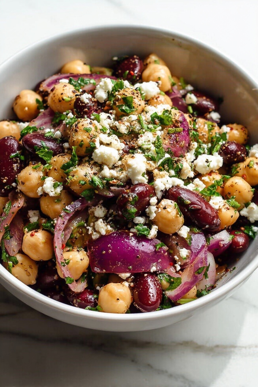 Healthy Chickpea Black Bean Salad, nutritious chickpea black bean salad, easy healthy salad, vegan bean salad, protein-packed vegetable salad - A white bowl filled with a salad showing three main layers: the bottom layer is a mix of beige chickpeas and dark red kidney beans; the middle layer includes large pieces of purple-red onion; the top layer is sprinkled with white crumbled cheese and small bits of bright green parsley, all mixed with visible black pepper and seasoning specks. The salad looks fresh and colorful, sitting on a white marbled surface, photo taken with an iphone --ar 2:3 --v 7