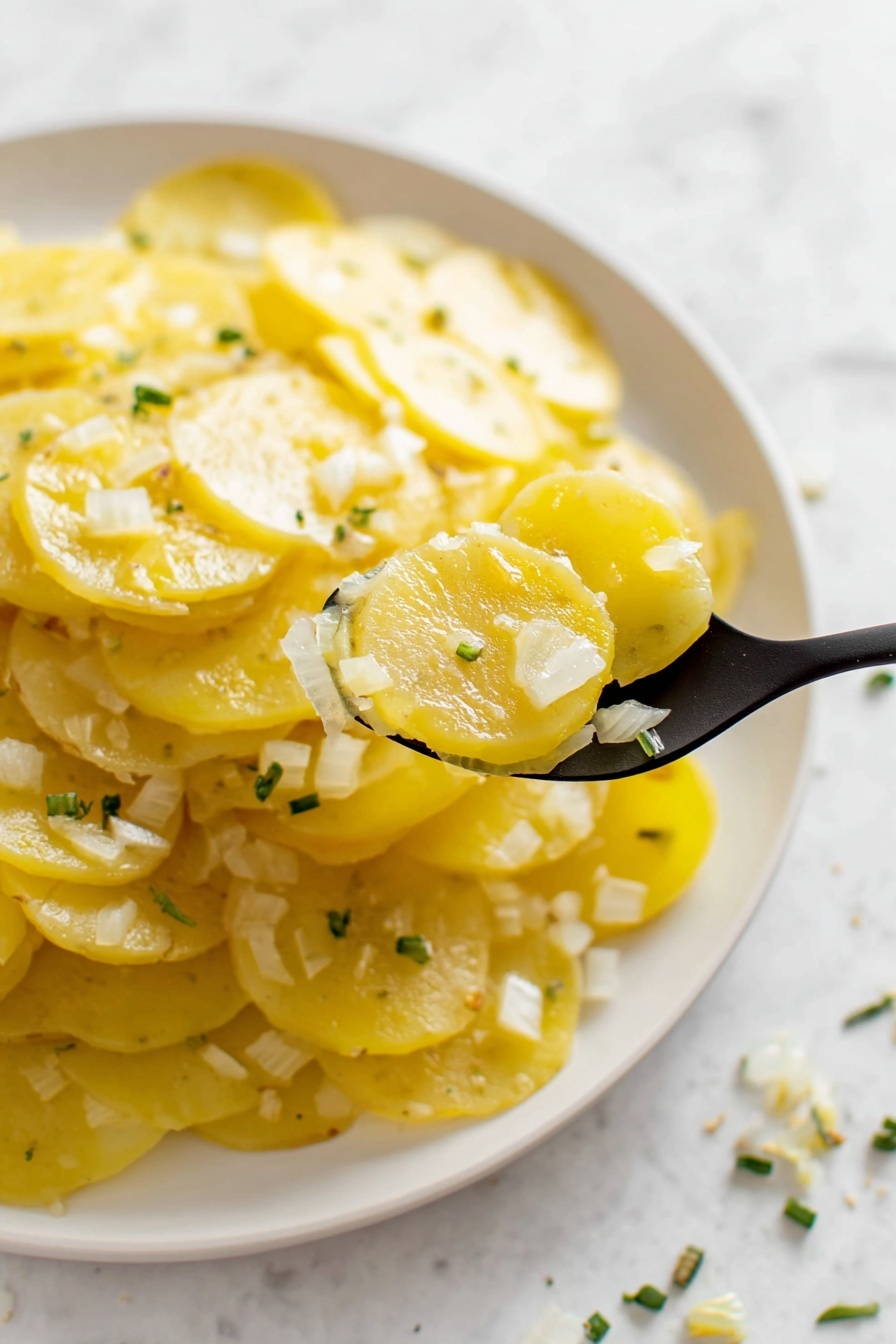 German Potato Salad, German Potato Salad Recipe, Tangy Potato Salad, Traditional German Potato Salad, Easy German Potato Salad - A close-up view of a white plate filled with thin yellow potato slices layered evenly across the plate, topped with small bits of white onion and tiny green herb pieces scattered lightly on top. A black spoon lifts a scoop of the potato and onion mix from the plate, showing the soft and slightly shiny texture of the potato slices. The background is a white marbled surface, and some of the green herbs are also scattered on it. The overall colors are soft yellow, white, and light green, creating a fresh, simple look photo taken with an iphone --ar 2:3 --v 7