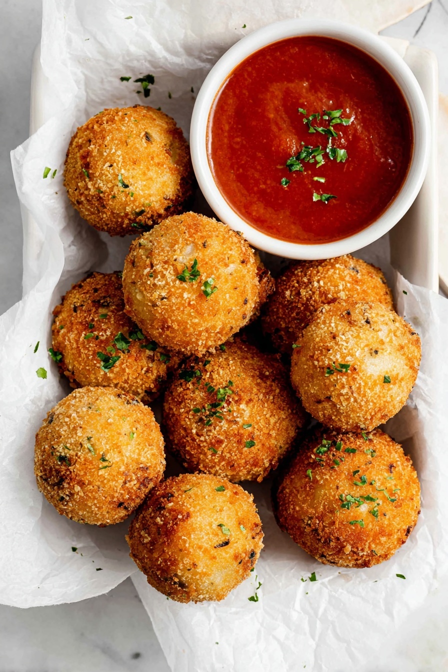 Crispy Potato Cheese Balls, cheesy snack recipes, crispy appetizer ideas, potato ball recipes, cheesy finger foods - There are nine golden brown, crispy round balls with a rough texture scattered on white parchment paper inside a white container. Each ball is sprinkled lightly with small bits of green herbs. To the top right of the balls, there is a small white bowl filled with smooth red sauce, garnished with tiny green herb pieces. The background shows a white marbled surface. Photo taken with an iphone --ar 2:3 --v 7