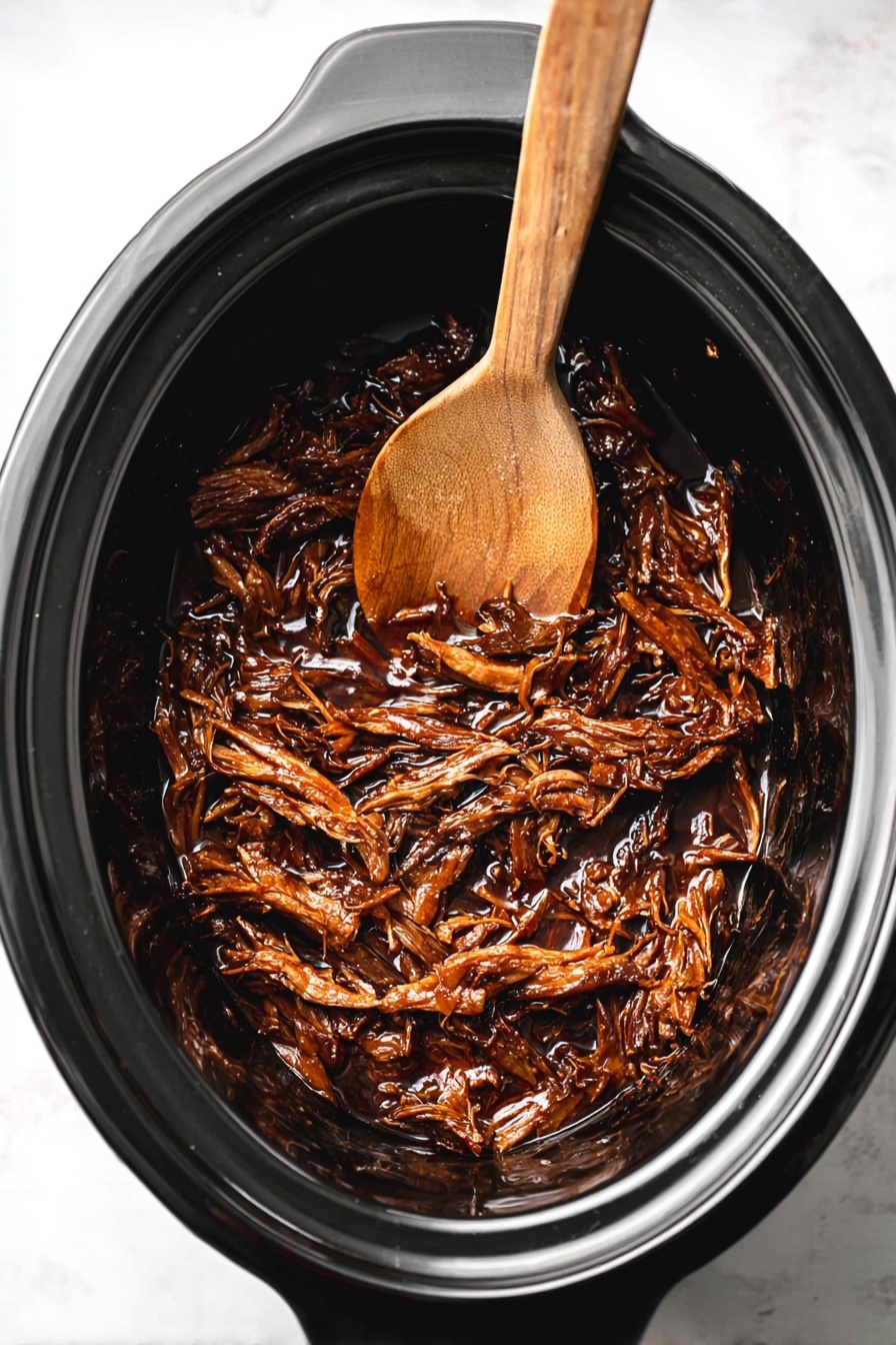 Slow Cooker Honey BBQ Beef Brisket, Honey BBQ Beef Brisket, Slow Cooker Brisket Recipe, Tender BBQ Beef, Easy Brisket Dinner - Inside a black slow cooker, there is a single layer of dark brown shredded meat with a shiny, sticky sauce coating it. Resting partially on top of the meat is a wooden spoon with a smooth brown texture. The slow cooker sits on a white marbled surface. photo taken with an iphone --ar 2:3 --v 7