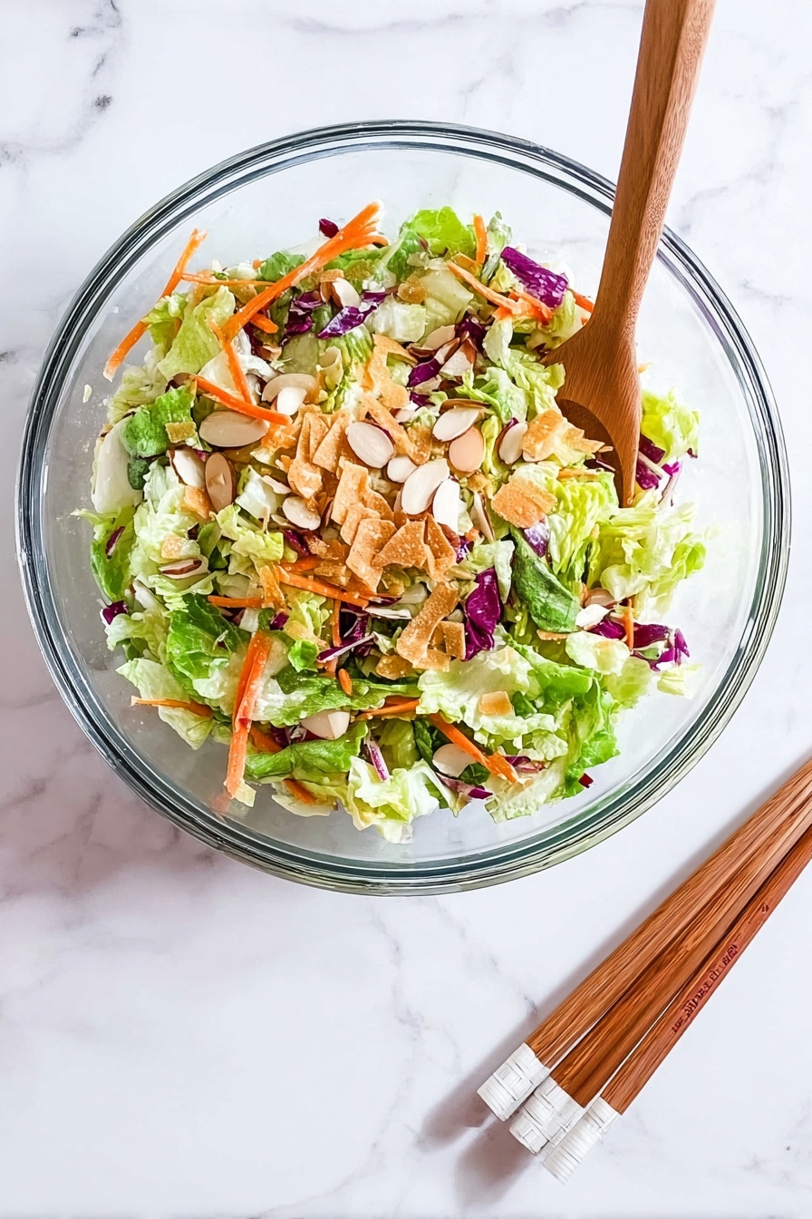 Crunch Chicken Salad on Crispy Egg Roll Base, Asian chicken salad recipe, crispy egg roll chicken salad, easy Asian salad with crispy shell, quick chicken salad appetizer - A clear glass bowl sits on a white marbled surface, filled with a colorful salad made of several layers: the bottom layer has bright green lettuce leaves mixed with light green cabbage, scattered on top are thin orange carrot strips and bits of purple cabbage, then sprinkled with light brown almond slices and thin crispy golden strips, creating a fresh and crunchy look. Beside the bowl, a pair of wooden chopsticks with white tips rests on the surface. photo taken with an iphone --ar 2:3 --v 7