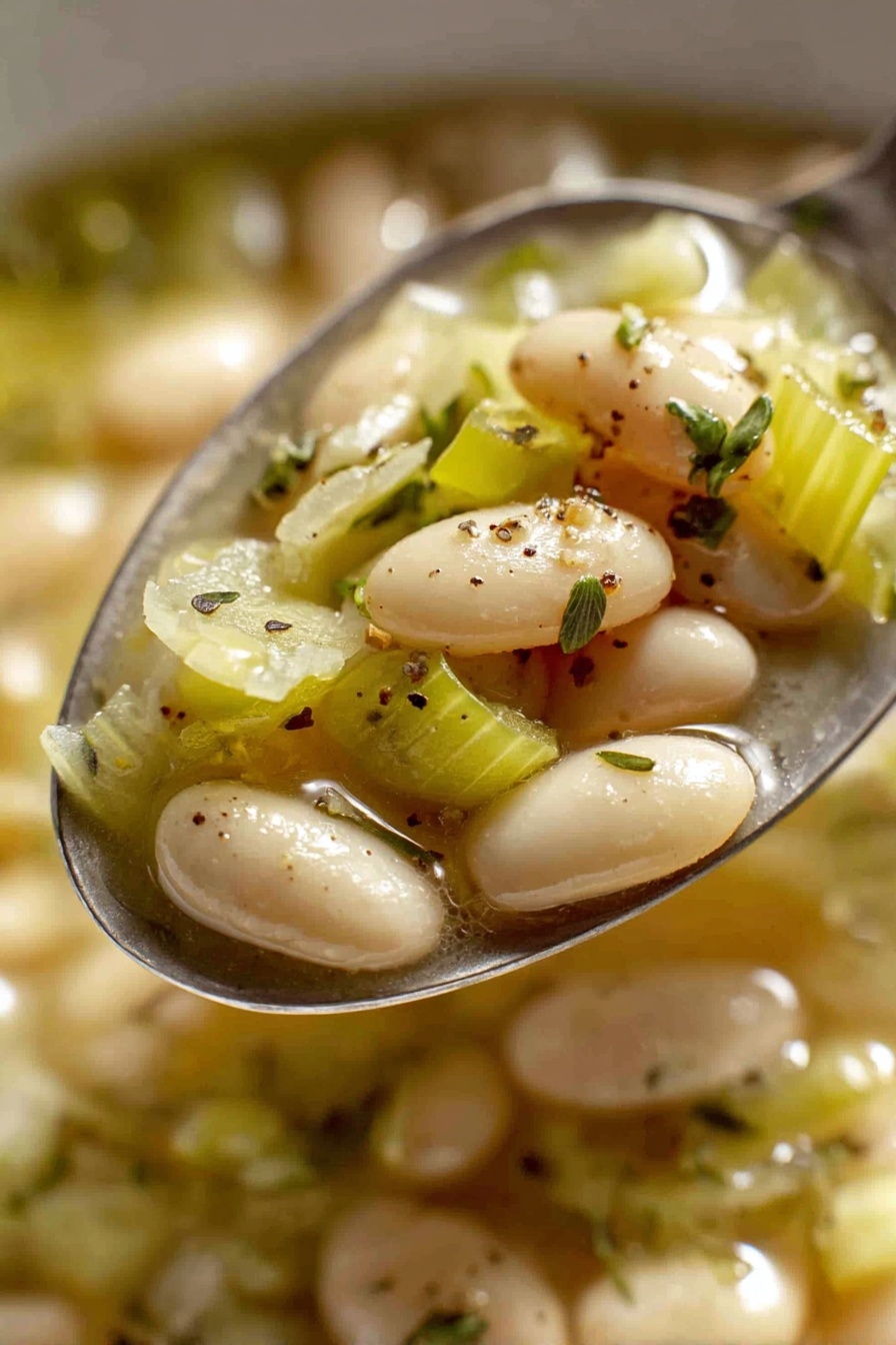 Creamy Butter Beans with Leeks, Creamy Butter Beans with Leeks recipe, easy vegan butter bean dish, hearty leek and bean main, comforting vegetarian meal - The image shows a close-up view of a red pot filled with a warm soup made of white beans and chopped green cabbage pieces in a light broth. The beans are smooth and oval-shaped, scattered evenly throughout the soup, while the cabbage is soft and lightly translucent with a pale green color. Small specks of black pepper and fresh thyme sprigs are sprinkled on top for garnish. The pot has a shiny red exterior with a white interior and two handles on the sides. The pot is sitting on a white marbled surface. Photo taken with an iphone --ar 2:3 --v 7