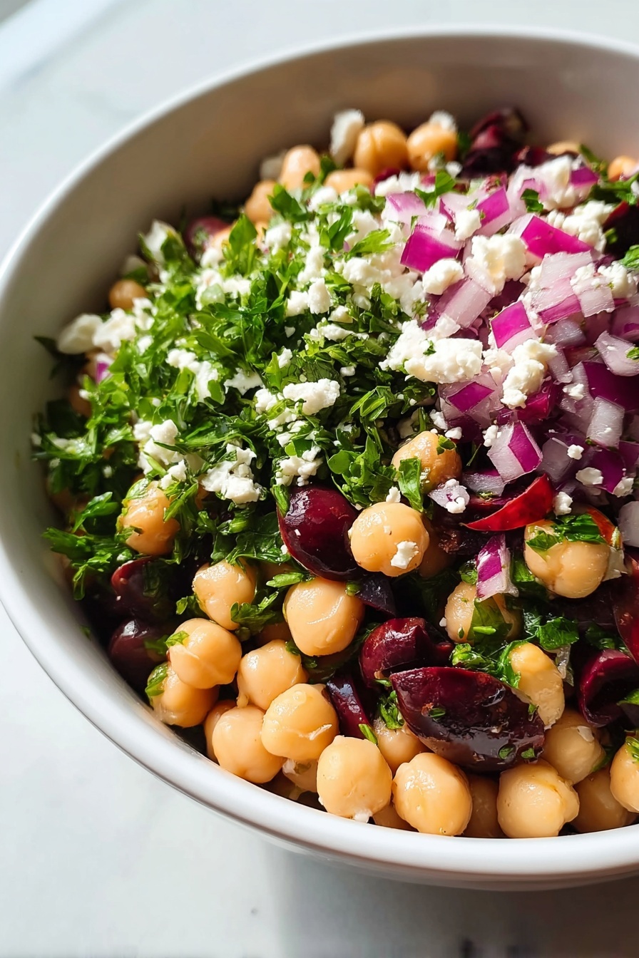 Healthy Chickpea Black Bean Salad, nutritious chickpea black bean salad, easy healthy salad, vegan bean salad, protein-packed vegetable salad - A close-up view of a white bowl filled with a colorful chickpea salad, showing roughly three layers. The bottom layer consists of smooth, round pale beige chickpeas mixed with dark purple olives. The middle layer has bright green chopped leaves, likely parsley, scattered throughout. The top layer is dotted with small white cheese crumbles and chopped purple-red onions, adding texture and vibrant color contrast. The bowl sits on a white marbled surface. photo taken with an iphone --ar 2:3 --v 7