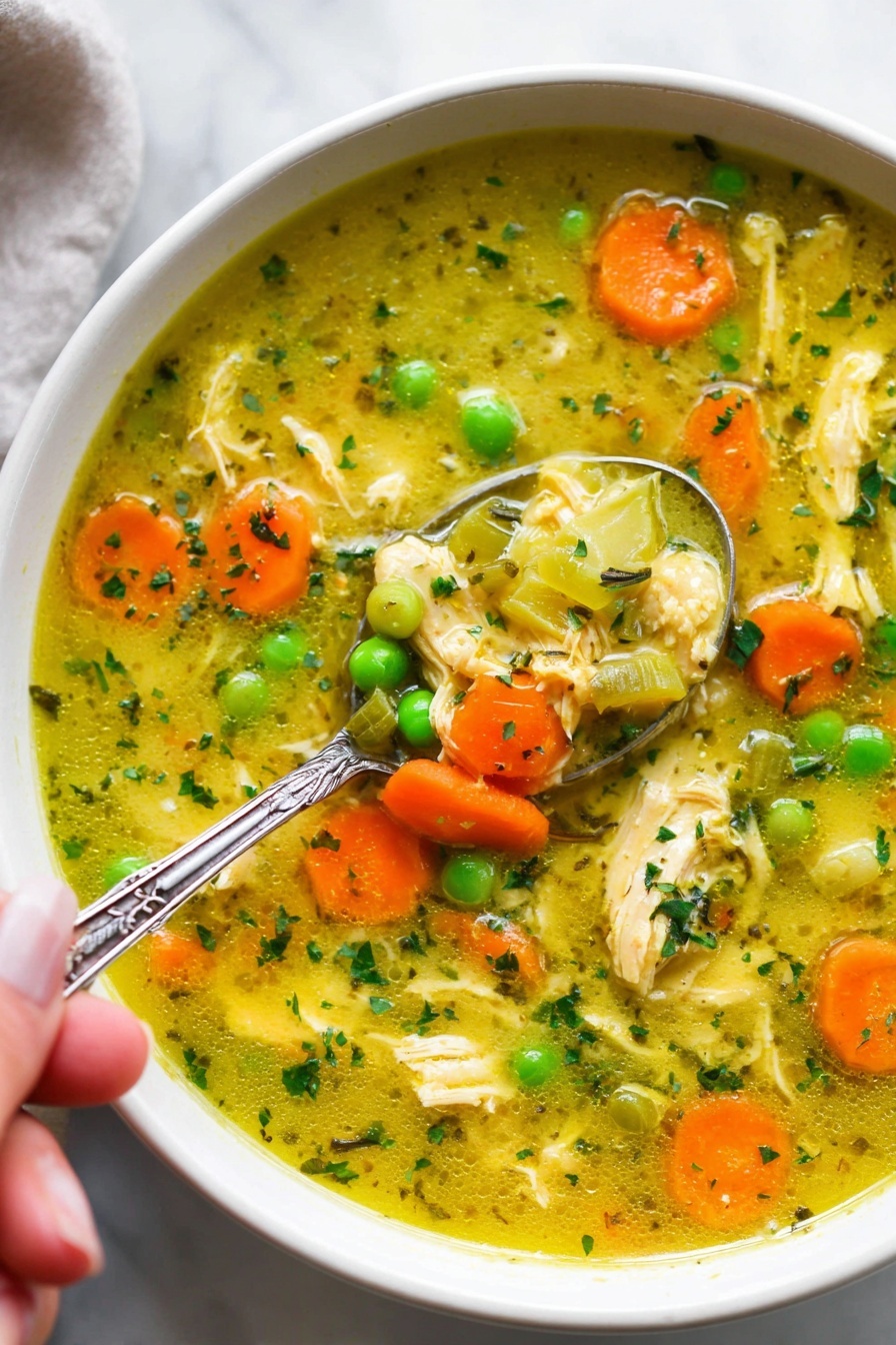 Turmeric Chicken Soup with Coconut Milk, turmeric chicken soup, healthy coconut milk soup, comforting chicken and turmeric broth, easy turmeric soup recipe - The image shows a white bowl filled with a colorful chicken soup. The soup has a yellowish broth with small pieces of shredded chicken scattered throughout. Bright orange carrot slices and vibrant green peas float on the surface along with translucent chunks of celery. Small green herb bits are sprinkled all over, adding texture and color. A silver spoon with detailing on the handle is partially submerged in the soup, held by a woman's hand, scooping some of the ingredients. The bowl sits on a white marbled surface, giving a clean and fresh look. photo taken with an iphone --ar 2:3 --v 7