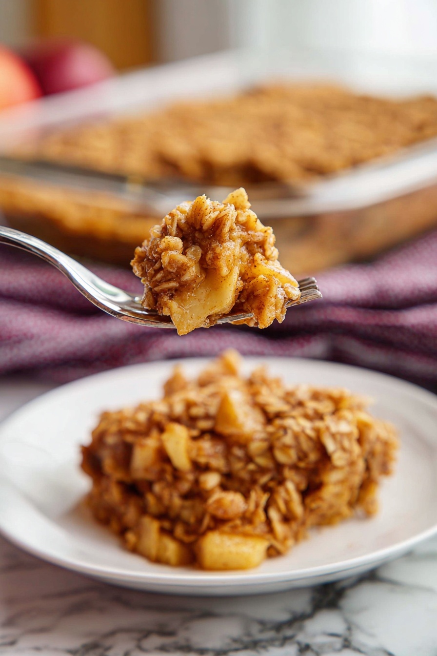 Apple Cinnamon Baked Oatmeal, cozy breakfast recipes, healthy breakfast ideas, quick oatmeal casserole, autumn breakfast favorites - A single square piece of oat crumble dessert sits in the center of a white plate with ridged edges. The dessert has two main layers: the top layer is golden brown with a rough texture made of baked oats mixed with cinnamon, while the bottom layer appears softer and darker, showing a moist filling beneath the oats. The plate is placed on a wooden table, and in the background, there is a glass baking dish with more of the same oat crumble. A dark red and white checkered cloth is also slightly visible behind the plate. Photo taken with an iphone --ar 2:3 --v 7