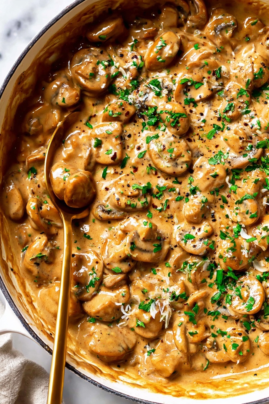 French Onion Pasta with Cheese, French Onion Pasta, cheesy pasta with caramelized onions, savory onion pasta dish, comfort food pasta recipes - The image shows a close-up of a white pan filled with creamy mushroom sauce. The sauce has many small round and sliced mushrooms in a thick, light brown sauce with visible black pepper and small bits of herbs. The top layer is sprinkled with fresh green chopped parsley. A brass-colored spoon is partially dipped in the sauce toward the left side of the pan. The pan is placed on a white marbled surface. Photo taken with an iphone --ar 2:3 --v 7