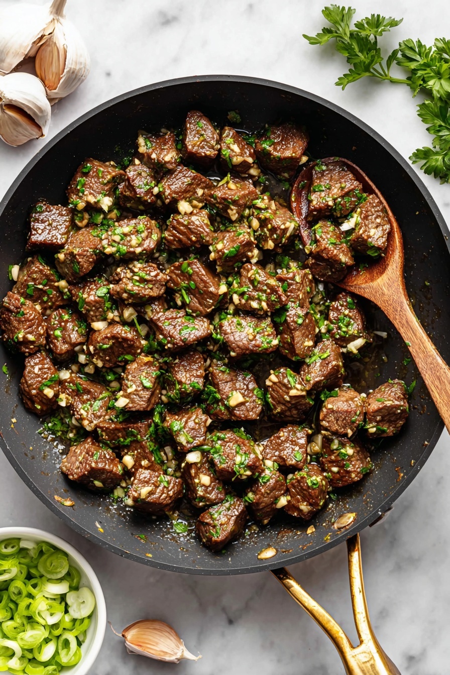 Garlic Butter Steak Bites, steak bite recipes, quick steak dinner, easy steak recipes, tender steak tips - The image shows a black pan filled with many small brown meat cubes cooked with small bits of white garlic and green parsley sprinkled on top, giving a fresh look. The pan has a golden handle at the bottom right, and a wooden spoon rests inside the pan on the right side, slightly lifting some meat. Around the pan, on a white marbled surface, there are two garlic cloves and a few green parsley leaves at the top left and a small white bowl filled with sliced green onions at the bottom left, adding color contrast. The overall look is warm and savory, with the textures of the meat and herbs clearly visible. photo taken with an iphone --ar 2:3 --v 7