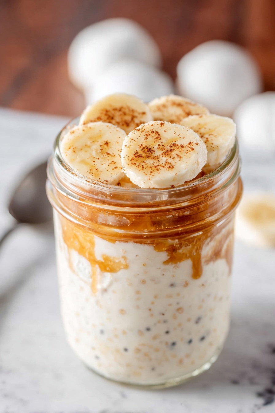 Peanut Butter Banana Overnight Oats, healthy overnight oats, quick breakfast ideas, easy make-ahead breakfast, nutritious breakfast recipes - A clear glass jar with a silver metal lid filled with three layers of overnight oats. The bottom layer is creamy white with tiny pieces of oats and seeds showing through. The middle layer has a light brown chunk inside the creamy oats mixture creating a rough texture. The top layer blends smoothly into the silver lid. The jar sits on a white marbled surface with scattered oats around, a white cloth on the left, and a yellow banana on the right photo taken with an iphone --ar 2:3 --v 7