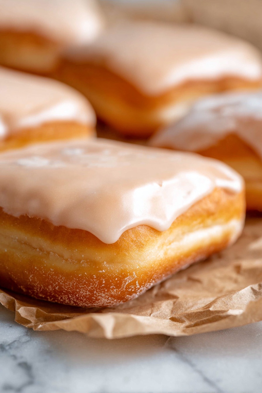 Maple Glazed Donut, homemade donut recipe, easy donut recipe, maple icing donuts, tender donut recipe - The image shows three rectangular pastries placed in a row on a long white plate. Each pastry is golden brown with a soft and slightly puffy texture. They are all covered with a smooth, thick, light caramel-colored glaze that drips slightly down the sides and pools a little at the base. The glaze has a shiny, glossy finish that highlights the warm color of the glaze and contrasts with the matte surface of the pastries beneath. The white plate is set on a light wooden surface. photo taken with an iphone --ar 2:3 --v 7